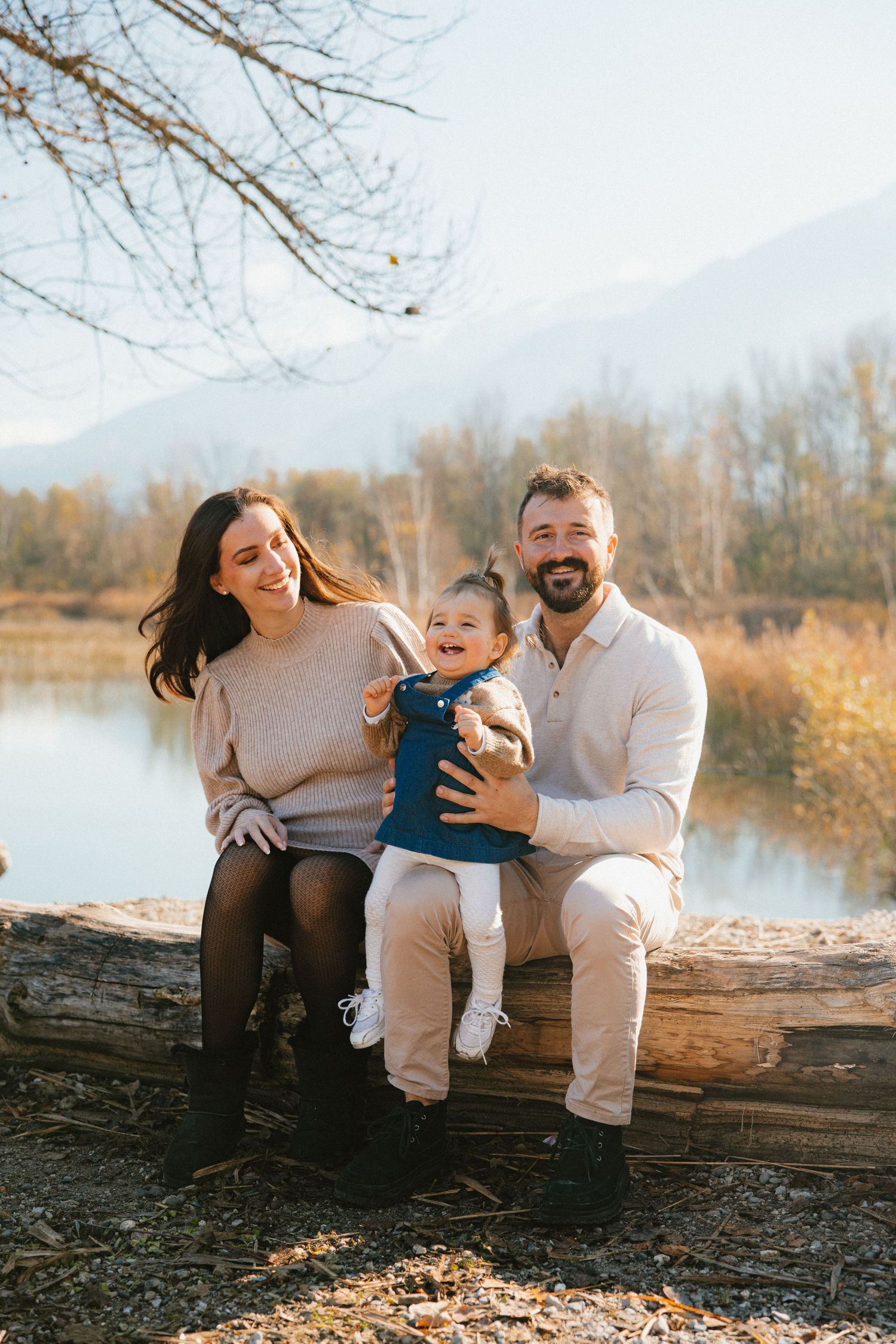 A family shares joyful moments while sitting together on a fallen log by a serene lake during golden hour.