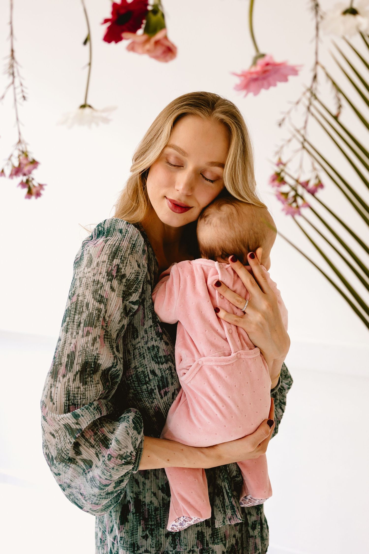 Sweet maternal moment with decorative flowers and palm leaves in a bright studio setting.