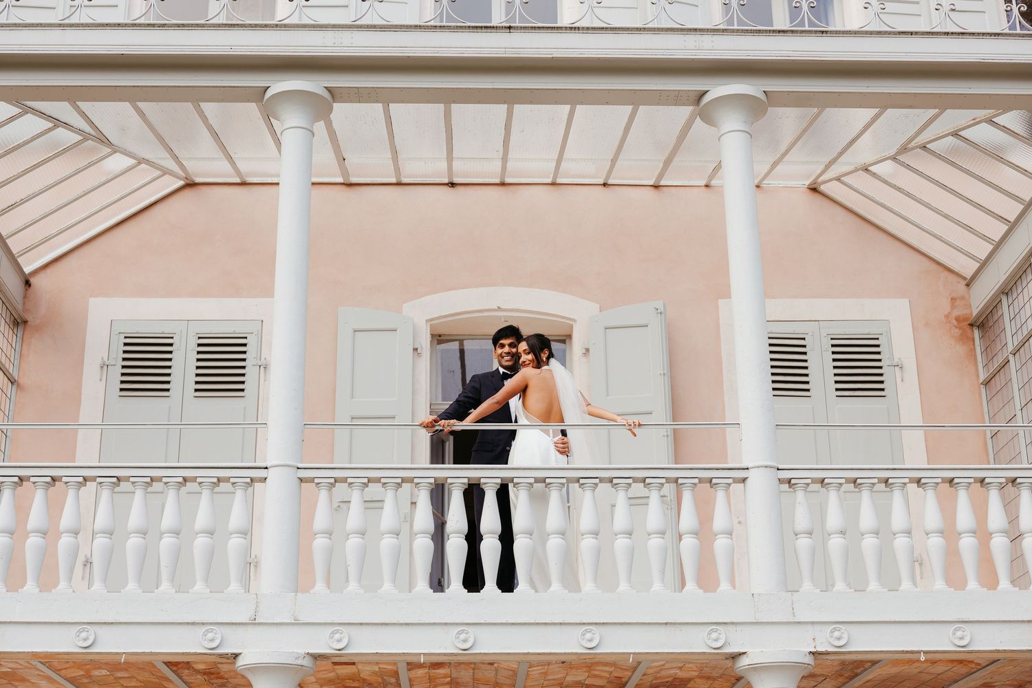 Couple celebrating on a white balcony of a colonial-style building.