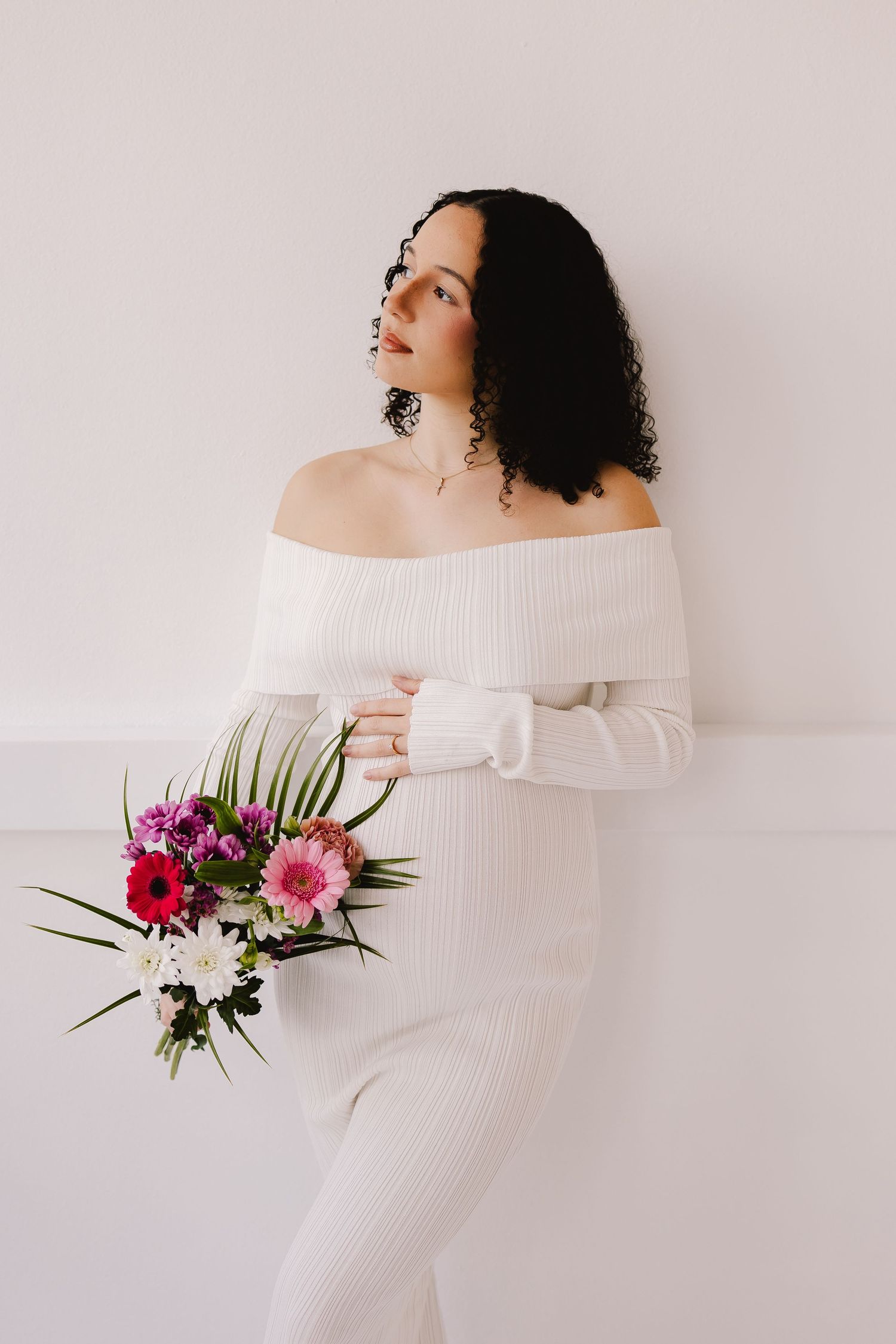 Maternity photo with white off-shoulder dress and vibrant floral bouquet.
