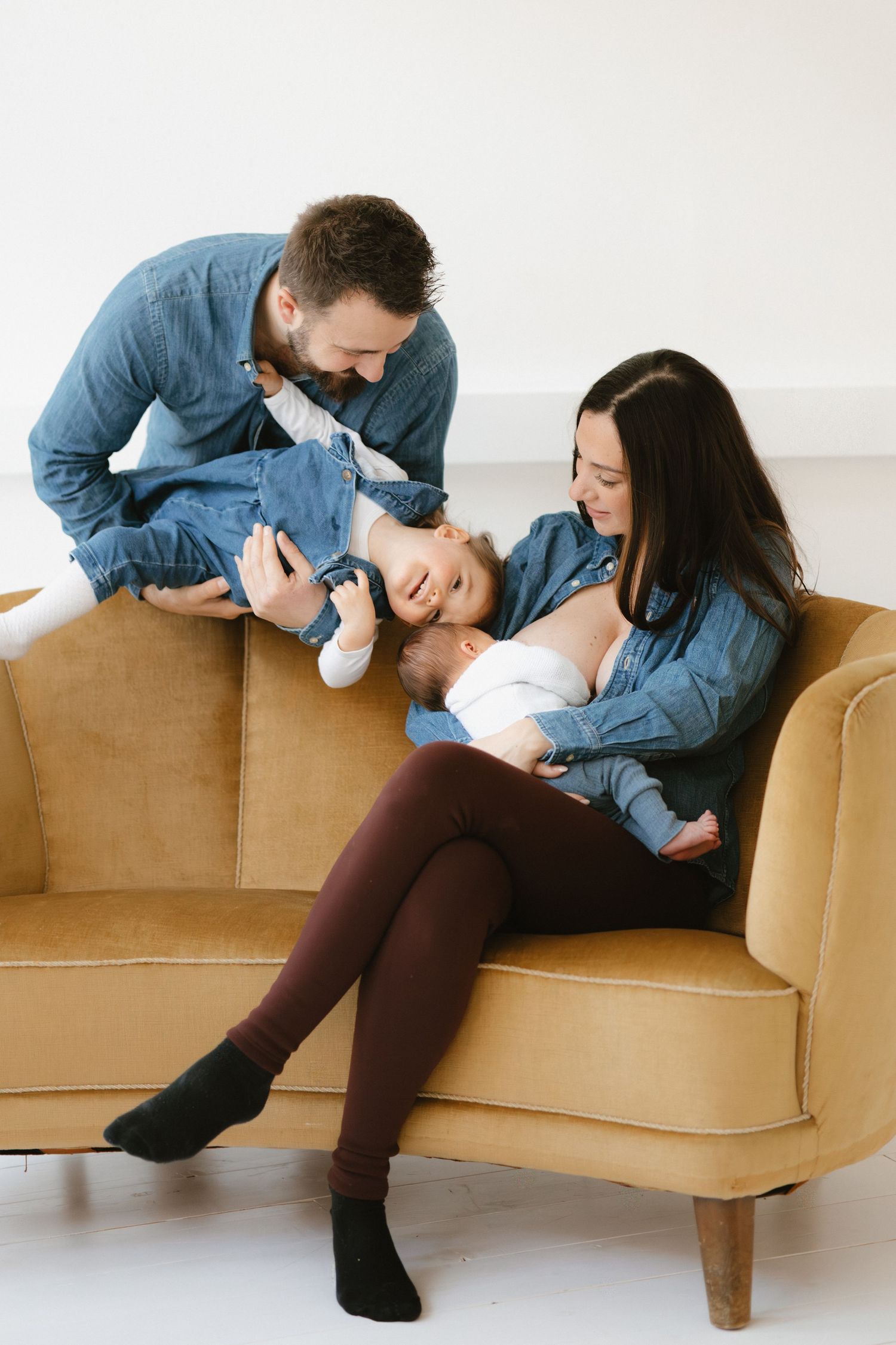 A family shares a tender moment together while relaxing on a tan couch, all wearing coordinating denim outfits.