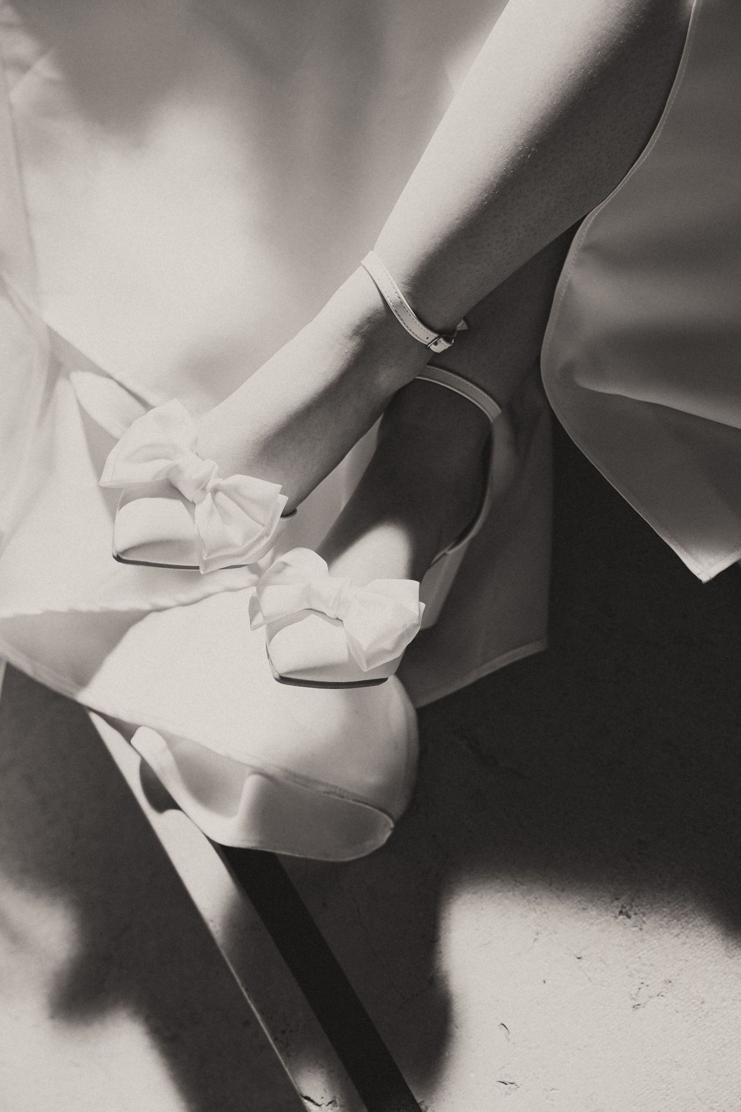 Close-up detail of elegant white bridal shoes in black and white photography.