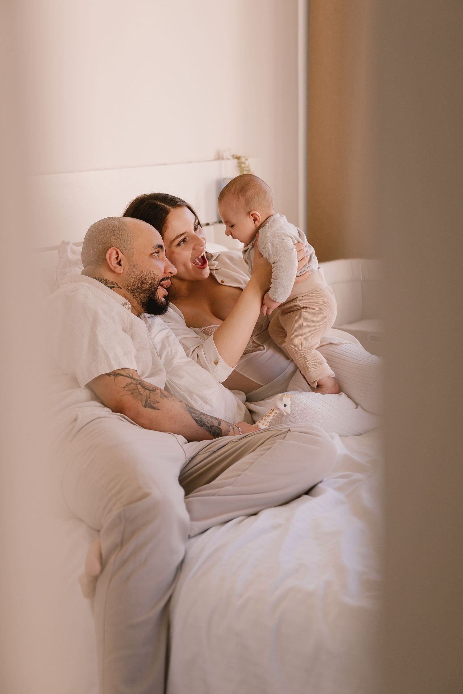 Tender family moments captured in soft lighting on white bedding.