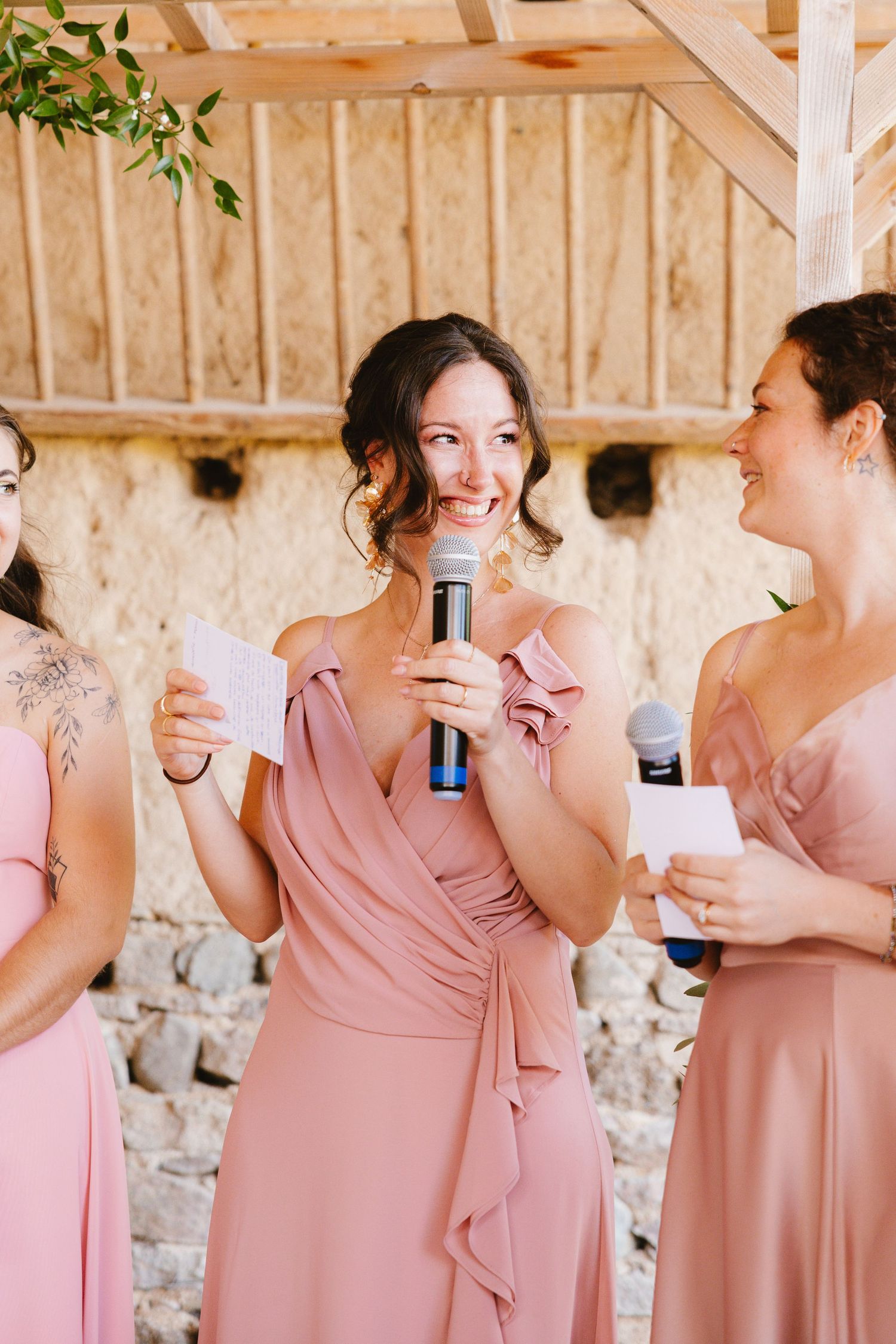 Bridesmaids in blush pink dresses share laughter and drinks during a candid wedding celebration moment.