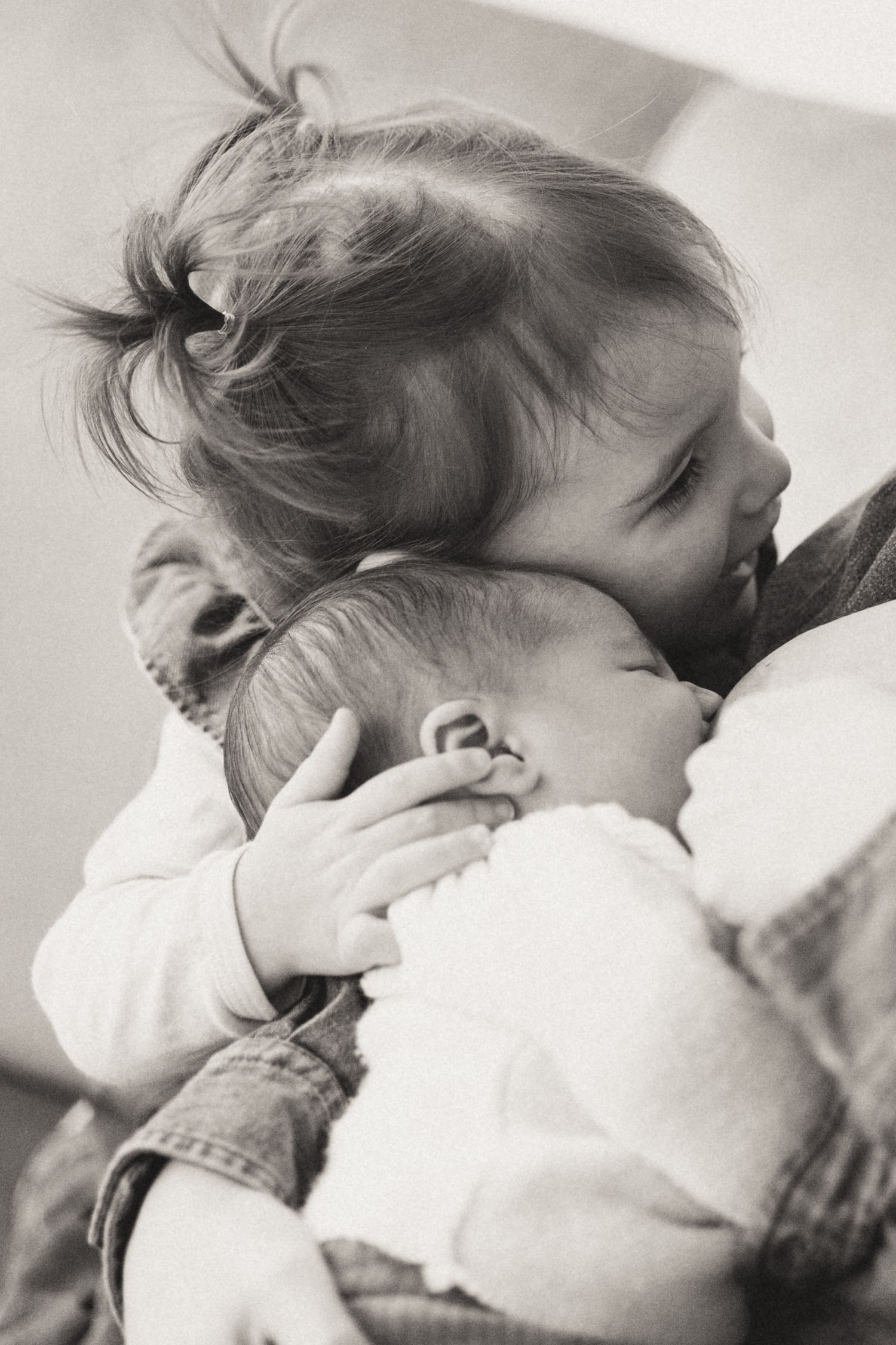 A tender black and white photograph showing a sweet embrace between a toddler and baby.
