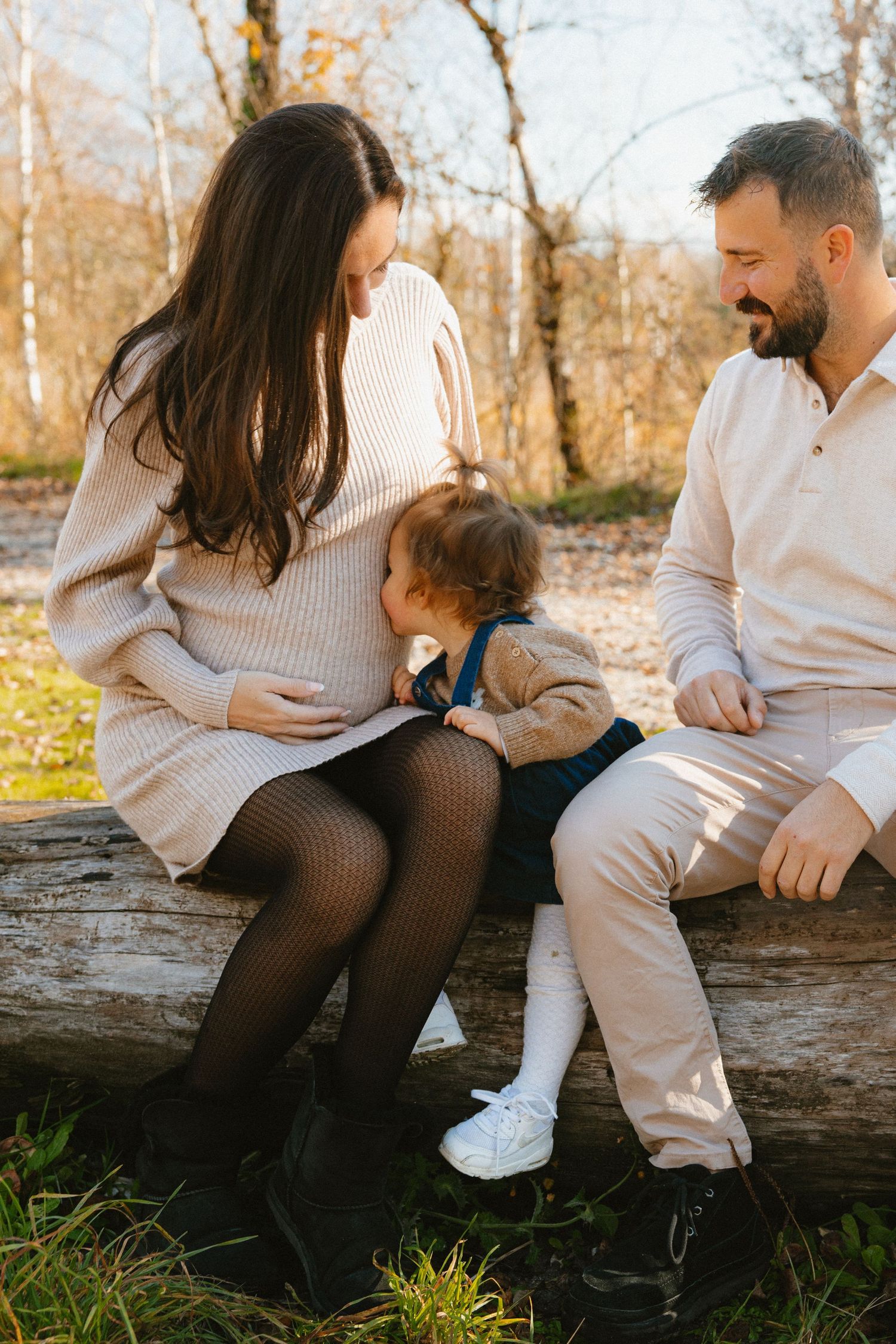 Family sitting together on fallen log in autumn forest wearing coordinated cream and white outfits.