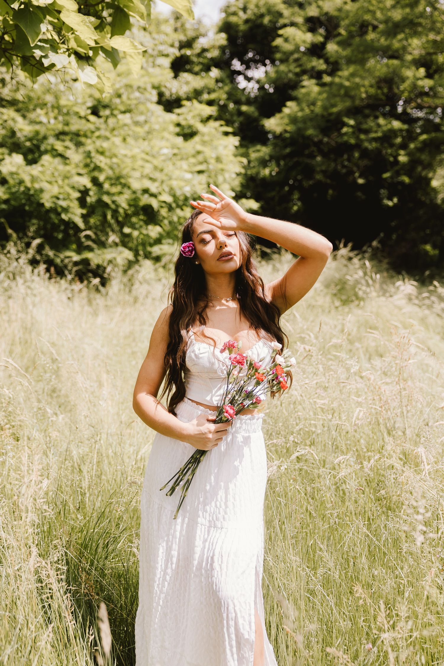 A ethereal summer portrait in a white dress holding wildflowers in a sun-drenched meadow.