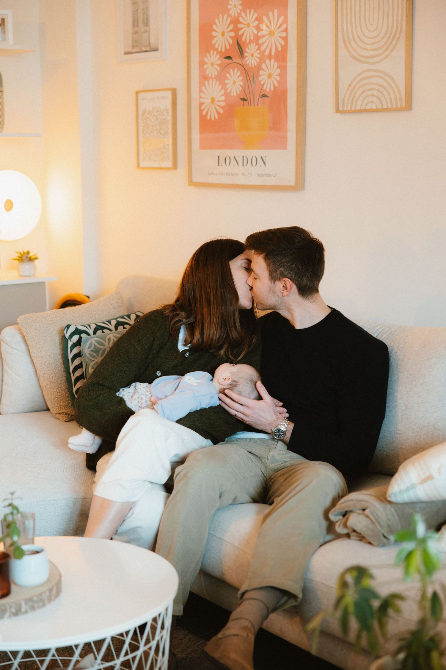Three cozy scenes show people relaxing together on a plush gray couch in a minimalist room with framed wall art.