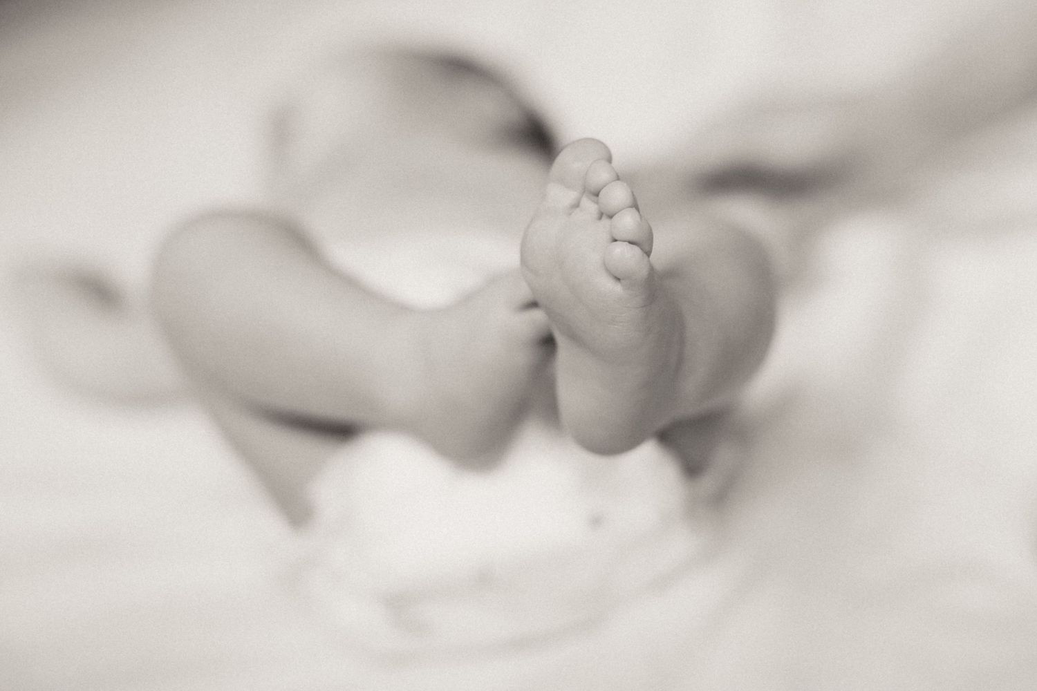 Tender baby feet details in soft focus create an intimate black and white newborn portrait.