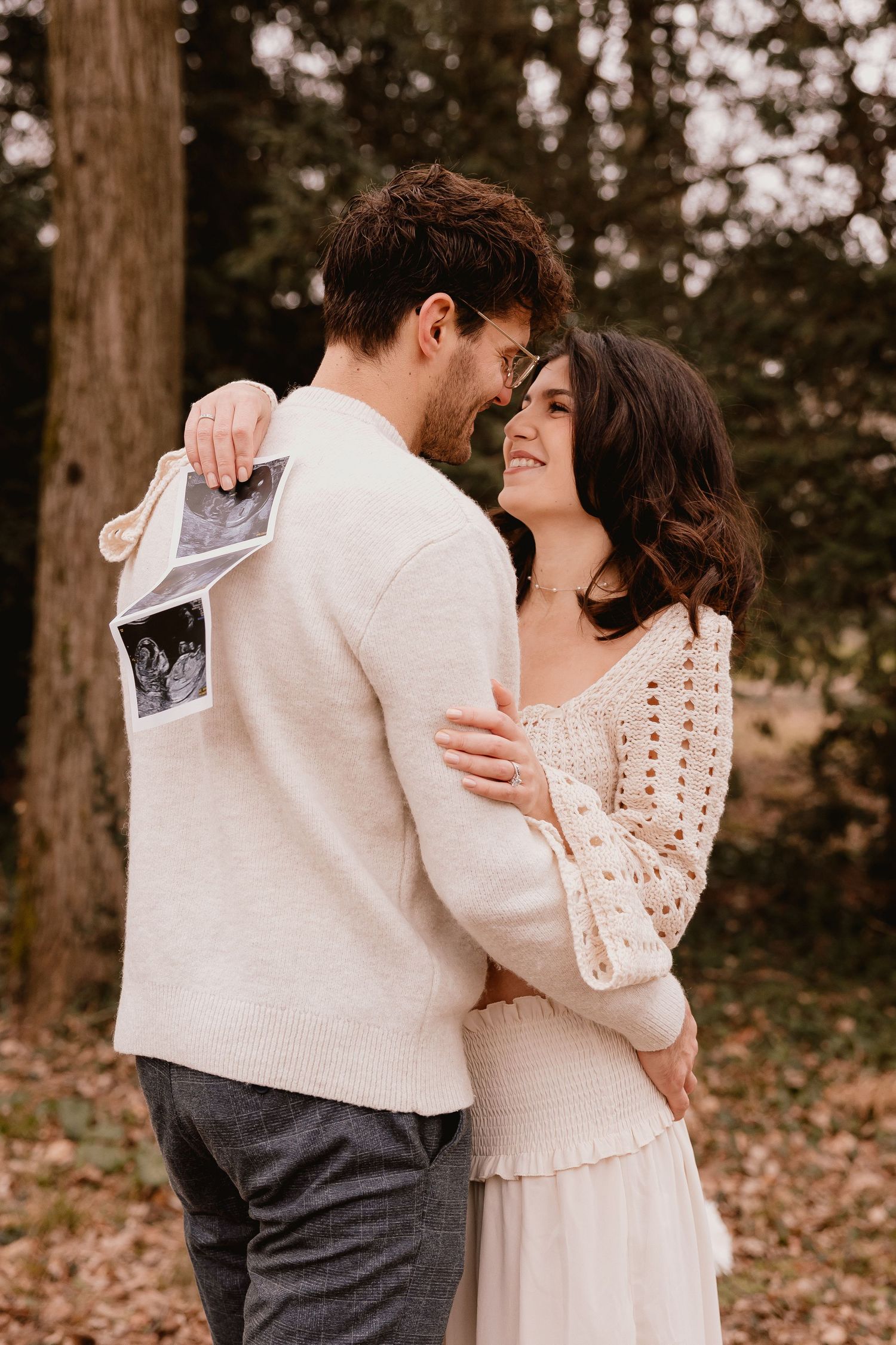 A couple embraces outdoors while holding an ultrasound photo, sharing a tender moment in autumn.