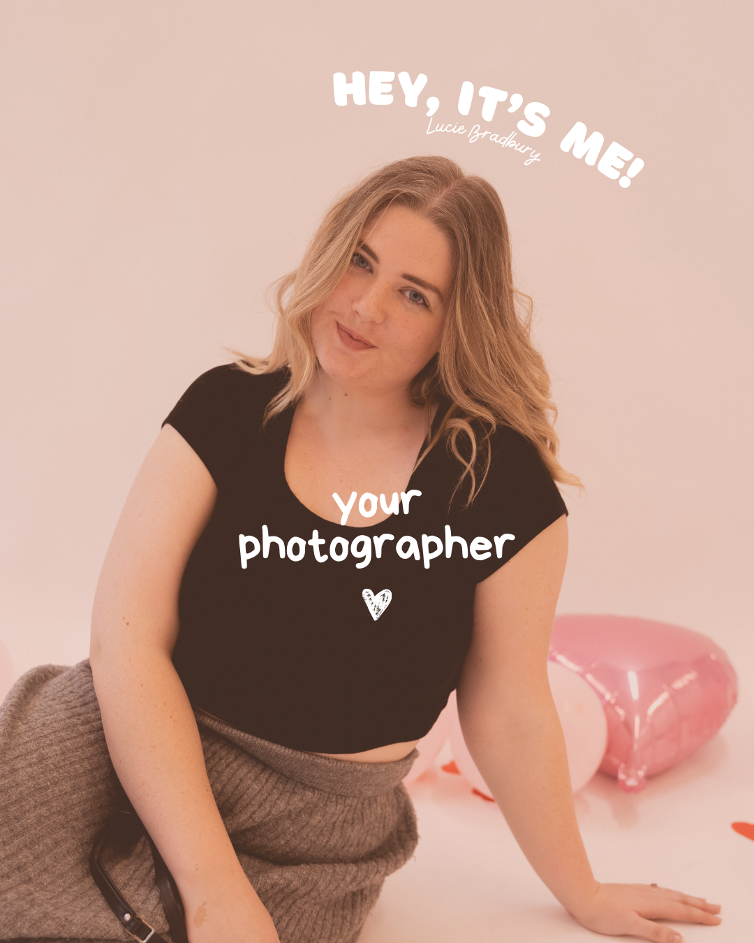 A young woman in a black crop top reading your photographer sits posed with pink heart balloons on a soft pink background.