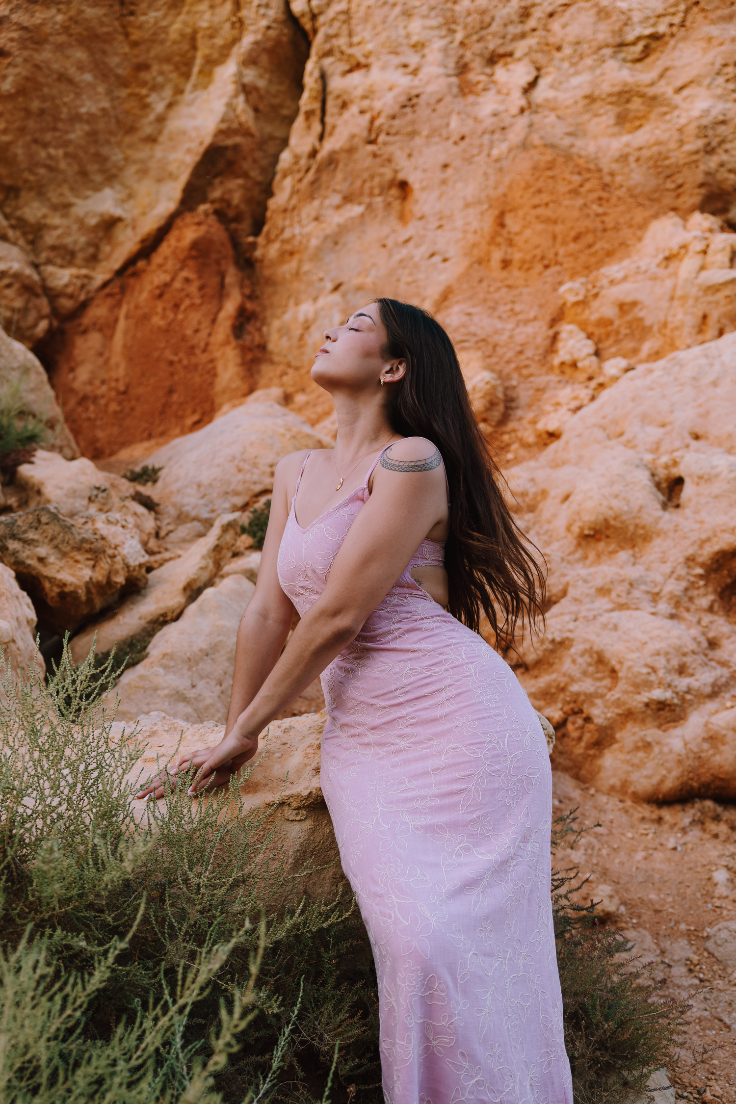 Person in pink dress poses dramatically against orange rock formations.