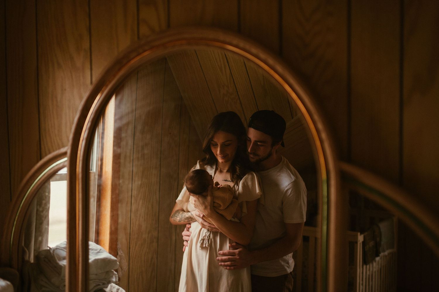 couple holding newborn baby in their home, photographed through the reflection of a vanity mirror