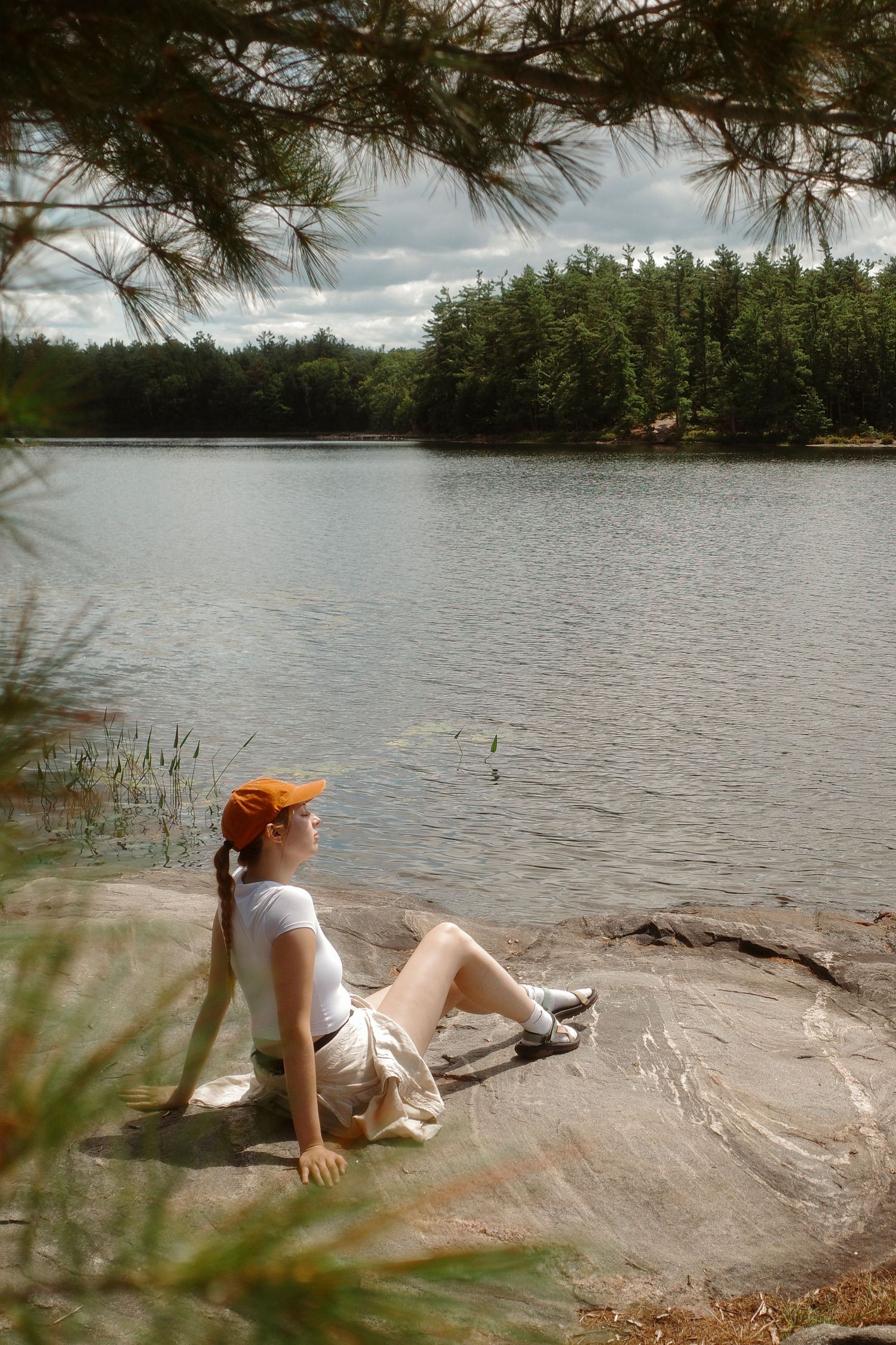 photographer Vanessa Hill sits by the water on a large rock with the sun on her skin