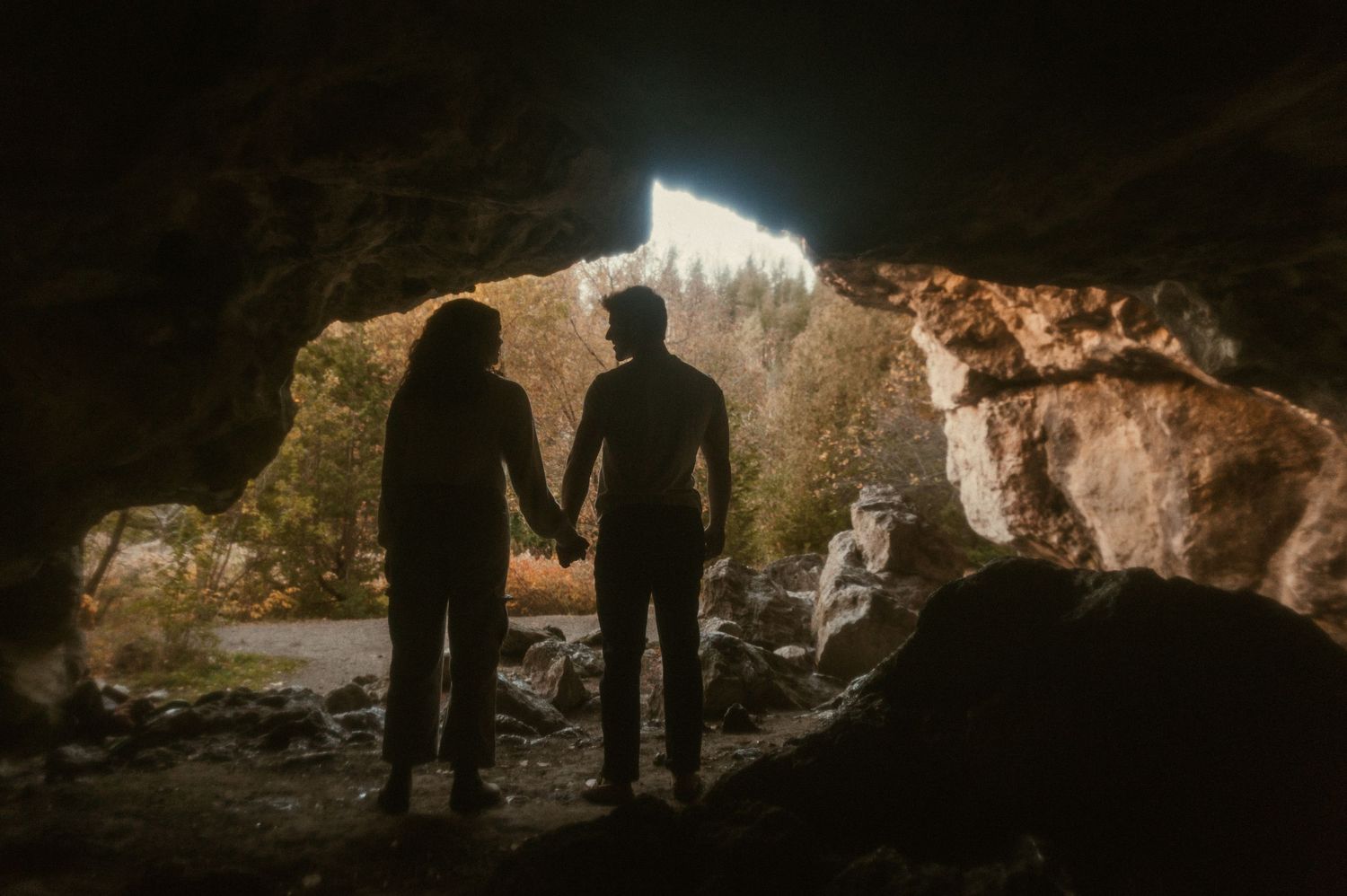 a couple holds hands while exploring a cave together