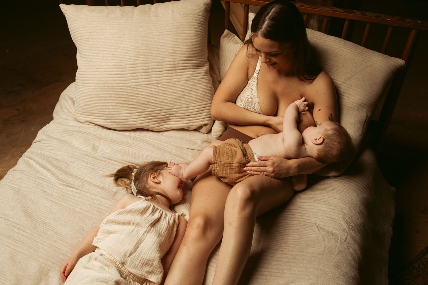 mother breastfeeds her son in bed while her daughter plays with her brothers toes