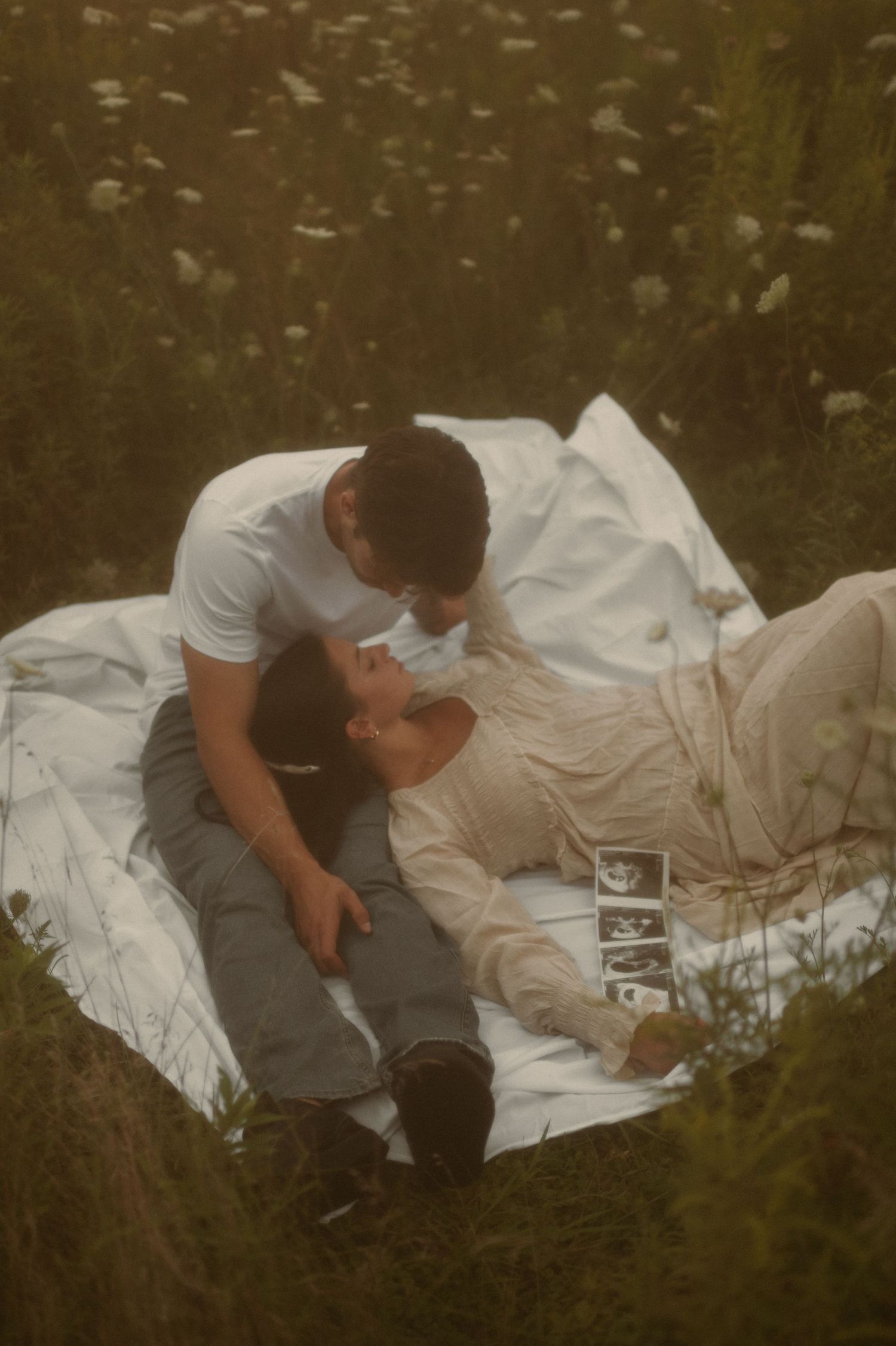 pregnancy announcement of a couple laying on a blanket in a flower field while holding a baby ultrasound