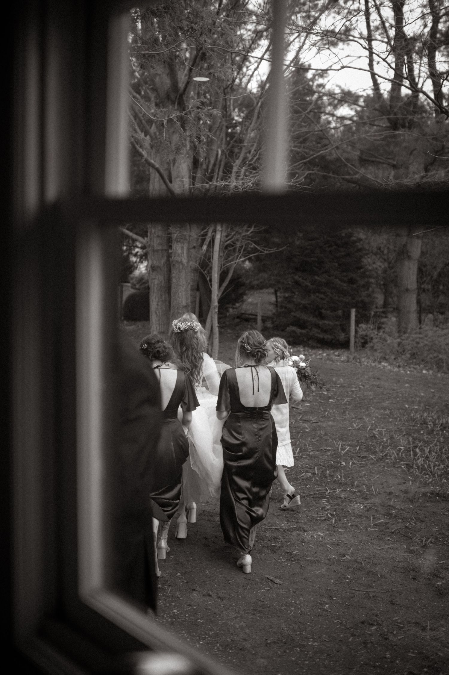 peering through the window to see a group of bridesmaids carrying the train of a bride, in black and white