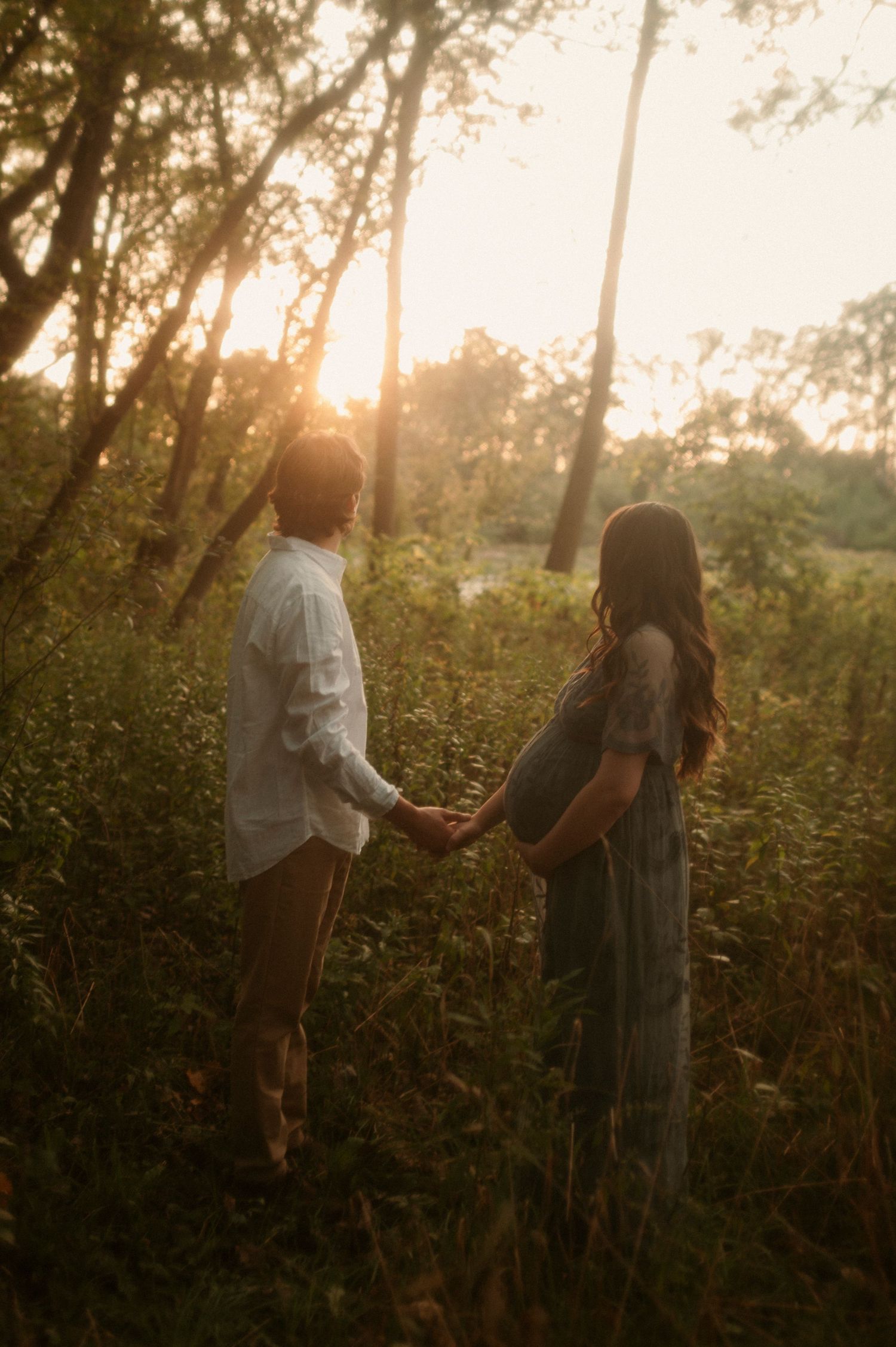 couple holding hands glancing off towards the sunset, the woman is pregnant and holding her belly bump. in brantford Ontario