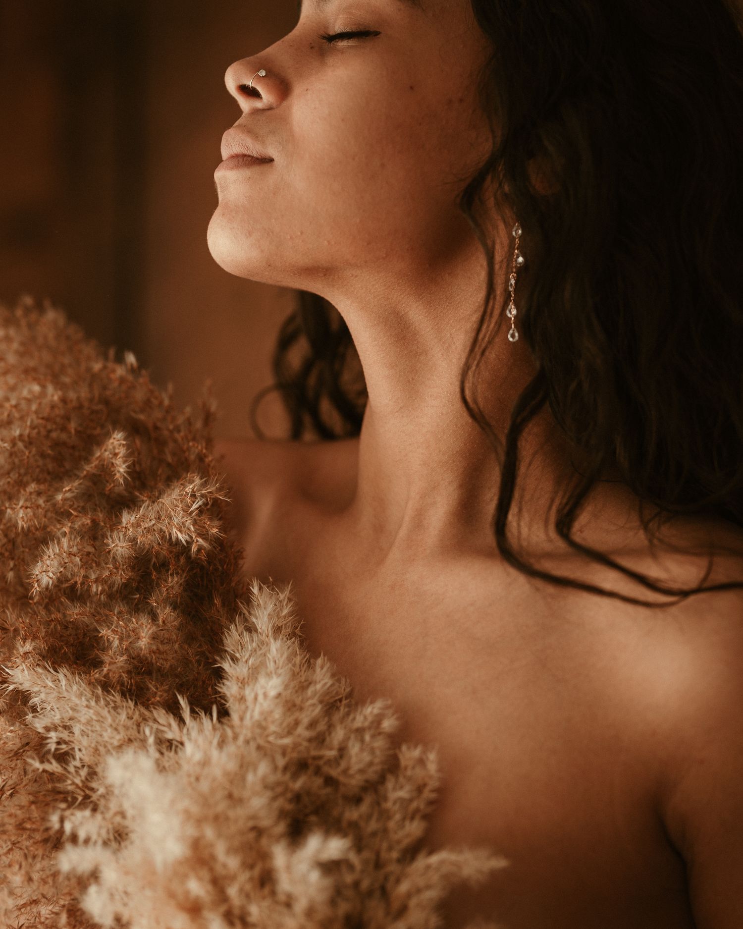 detail of a woman's bare chest and neck, she holds a bouquet of dried florals to cover herself