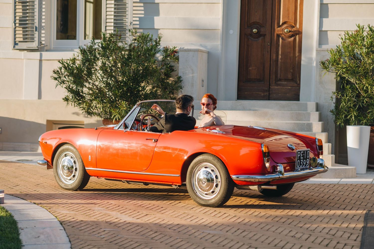 Classic red vintage Alfa Romeo convertible sports car parked in front of an elegant white building entrance.