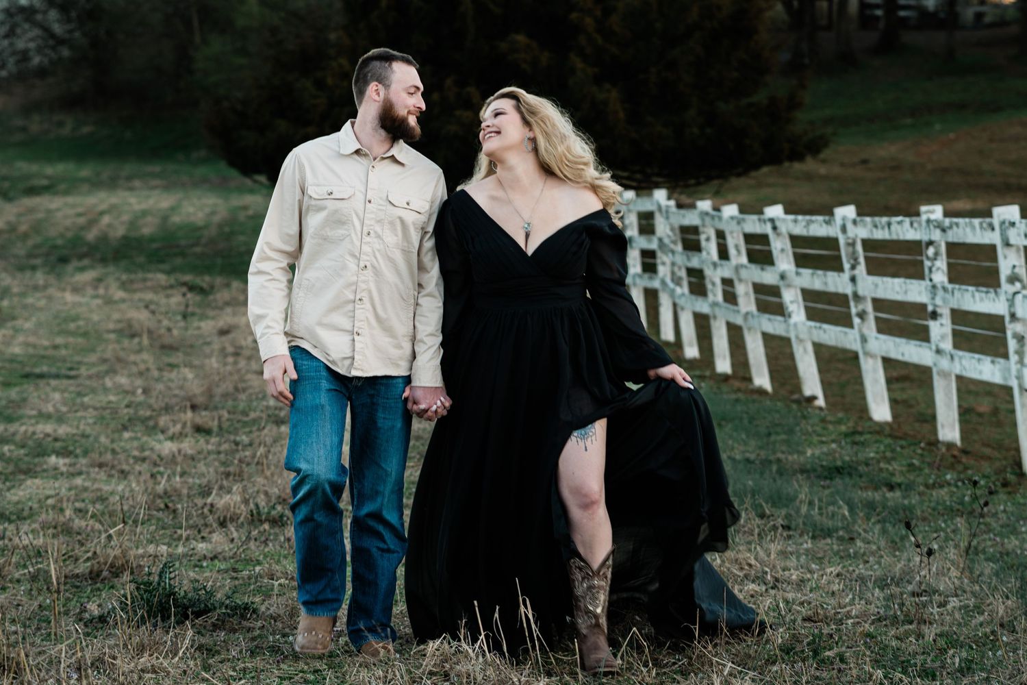 Couple posing together against wooden fencing in a romantic countryside setting at dusk.
