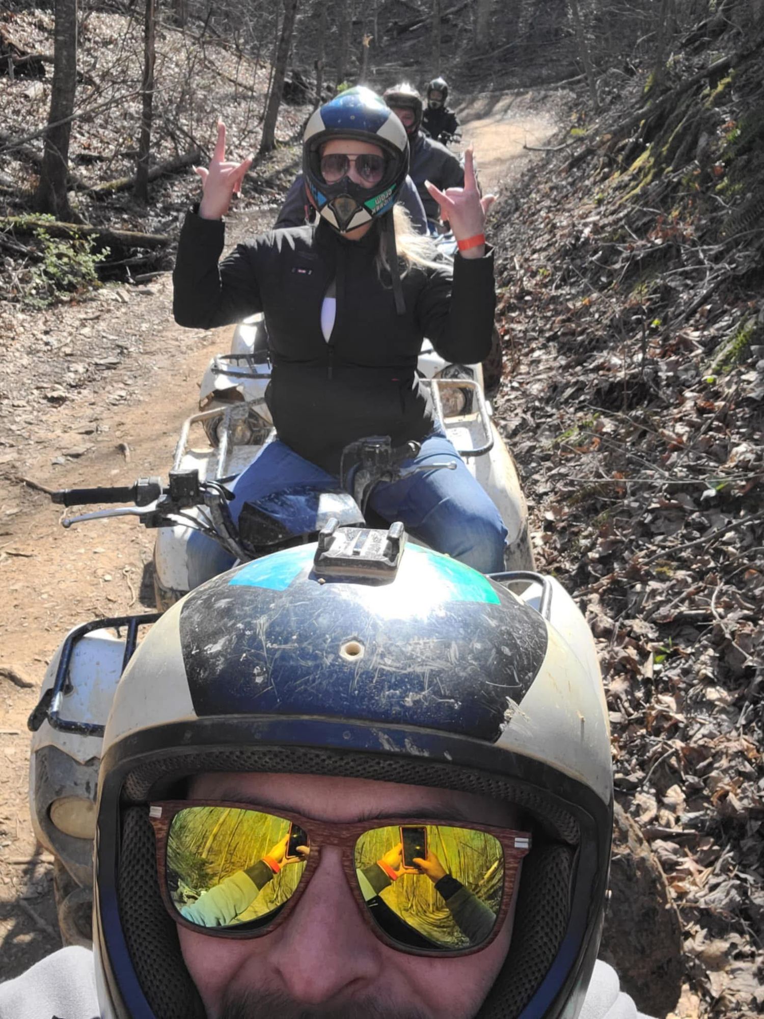 A series of four selfie photos showing a person in helmet and sunglasses riding an ATV on a wooded trail.