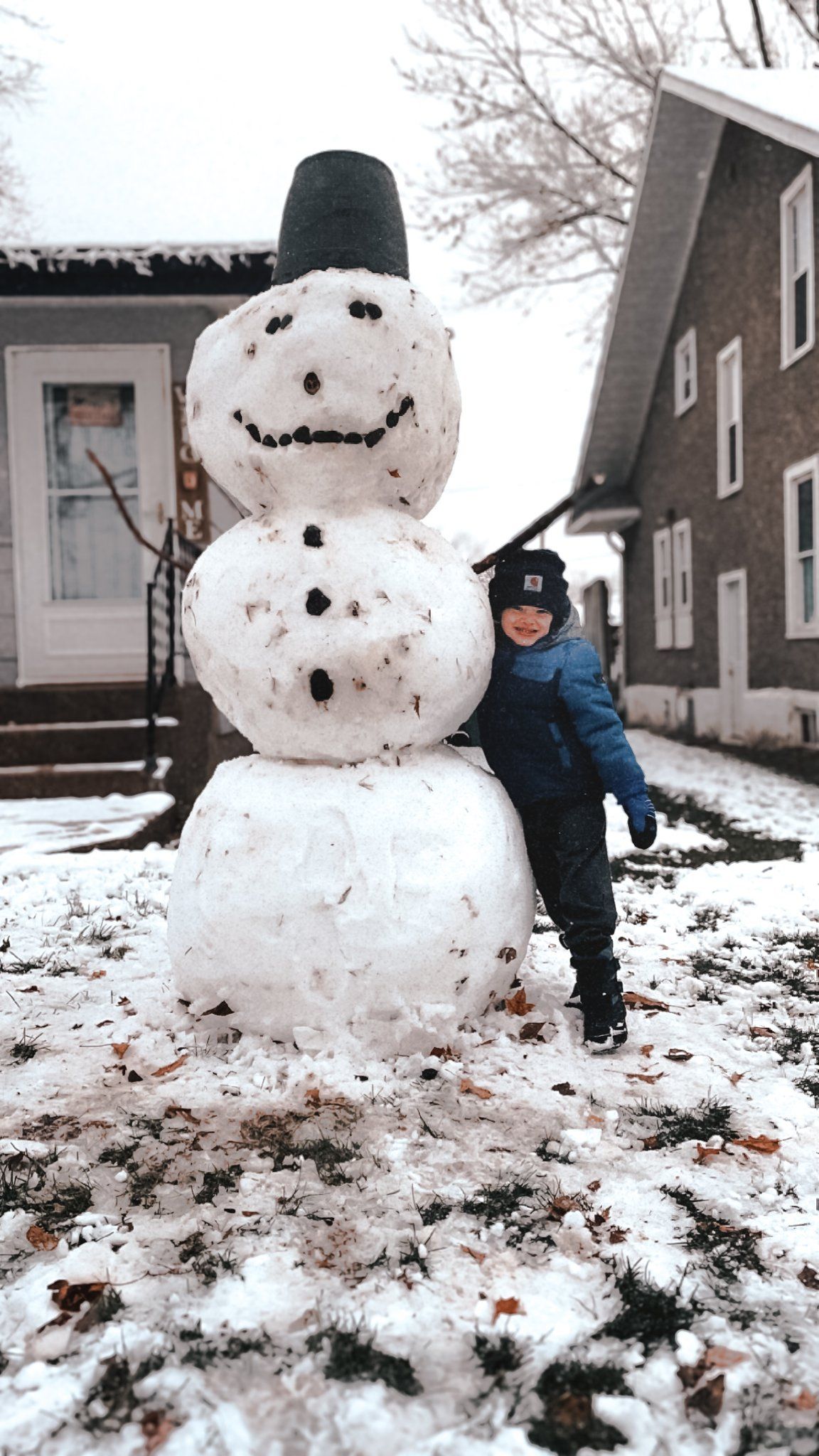 Building a snowman sequence in winter with dark houses in background.