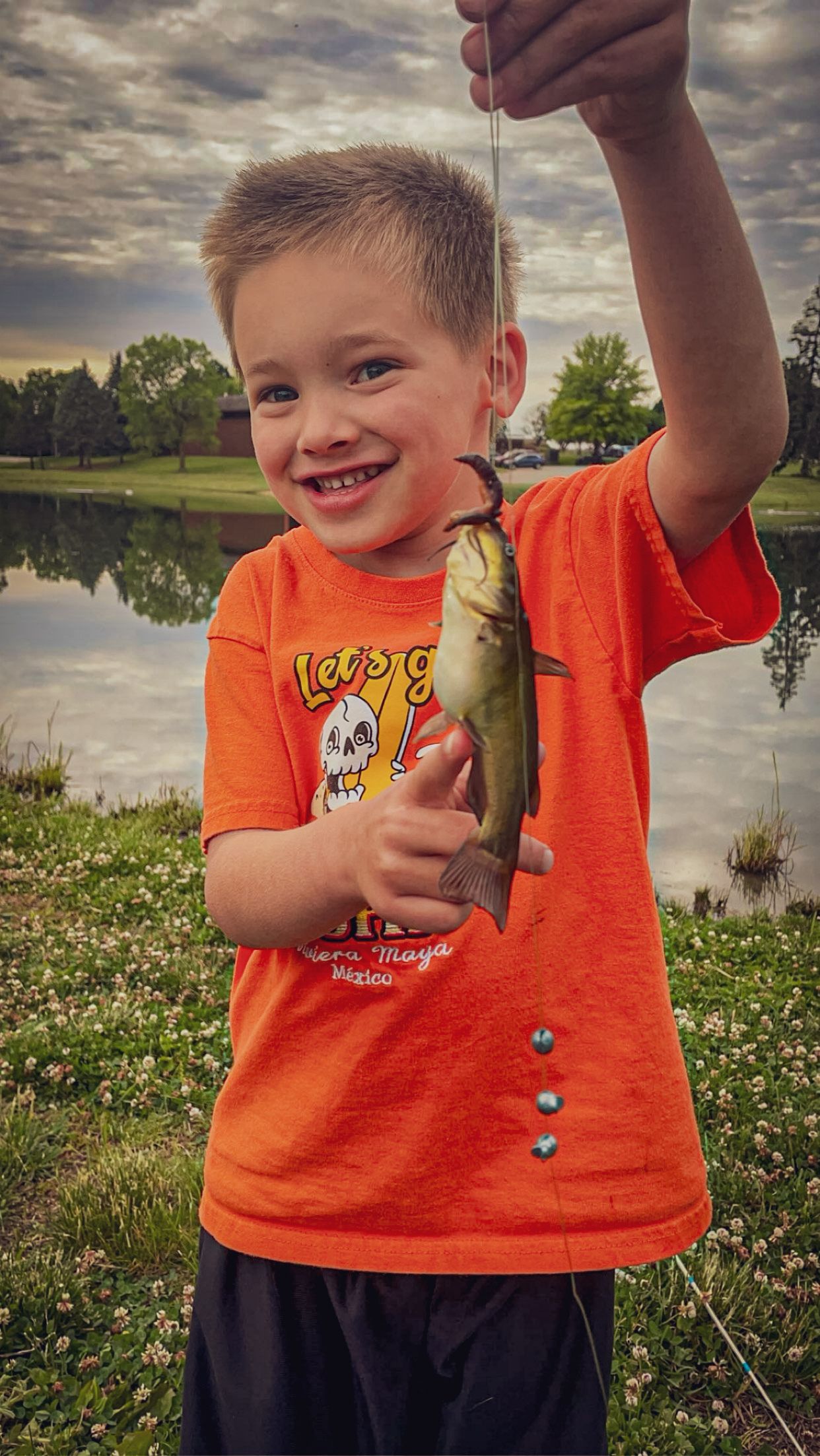 Proud catch of a small fish by a lake on a cloudy evening.