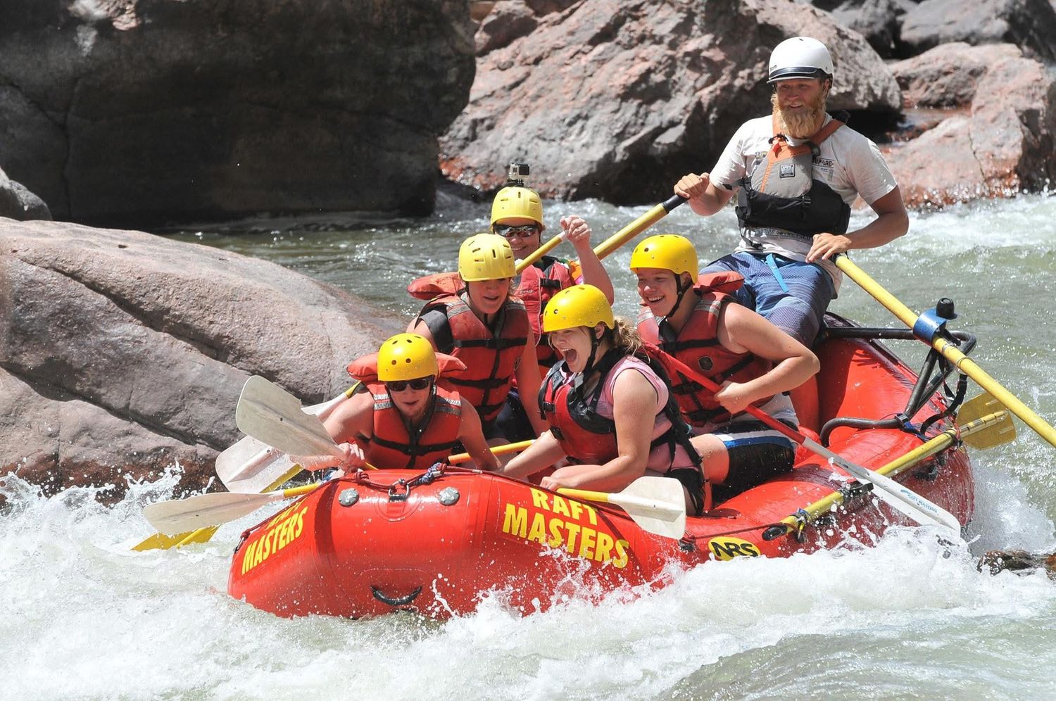 Group whitewater rafting through rapids in a red inflatable raft.
