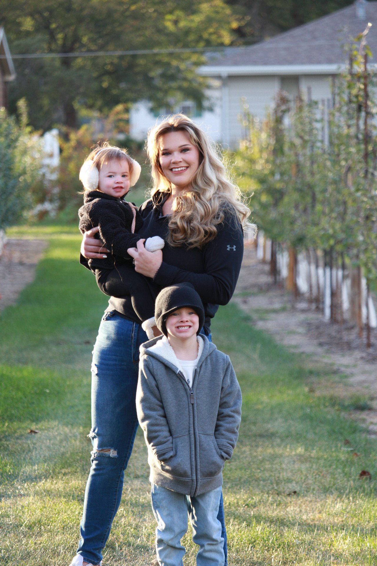 Three candid outdoor photos show a playful family moment with a small group posing on grass near a row of trees.