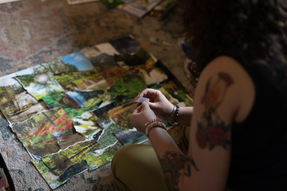 Someone creating a collage by arranging torn magazine pieces on a surface while taking notes with a pen.