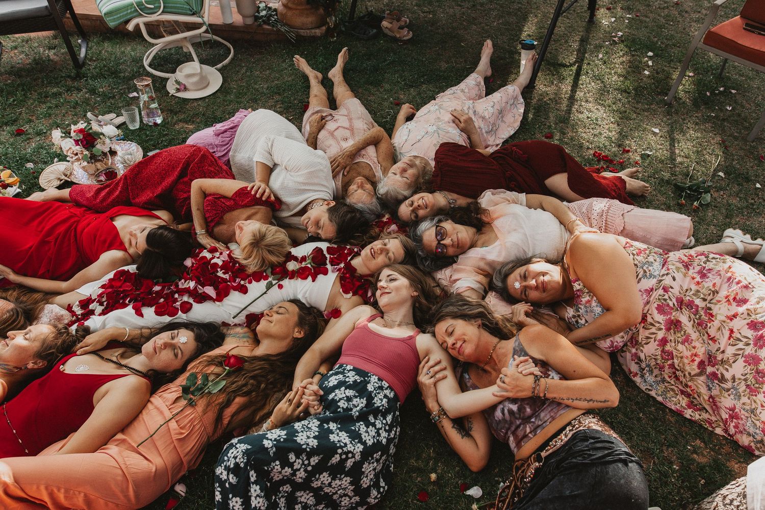 A group lies in a circle on blankets in a garden setting while enjoying a summer afternoon together.