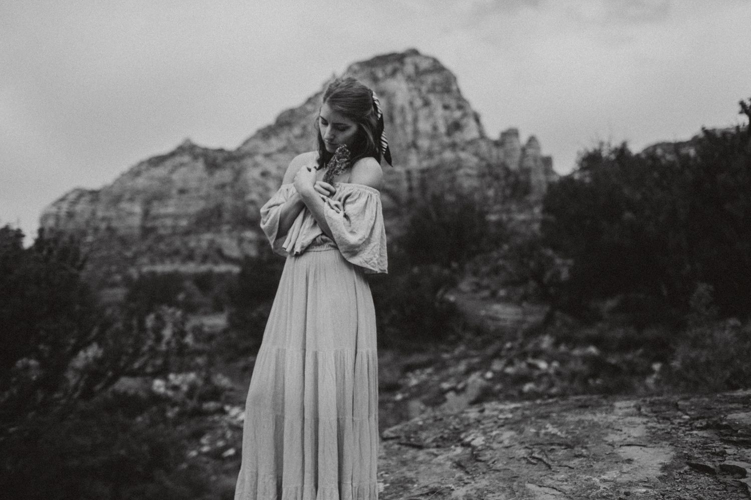 Artistic black and white portrait of person in flowing dress against mountain scenery.