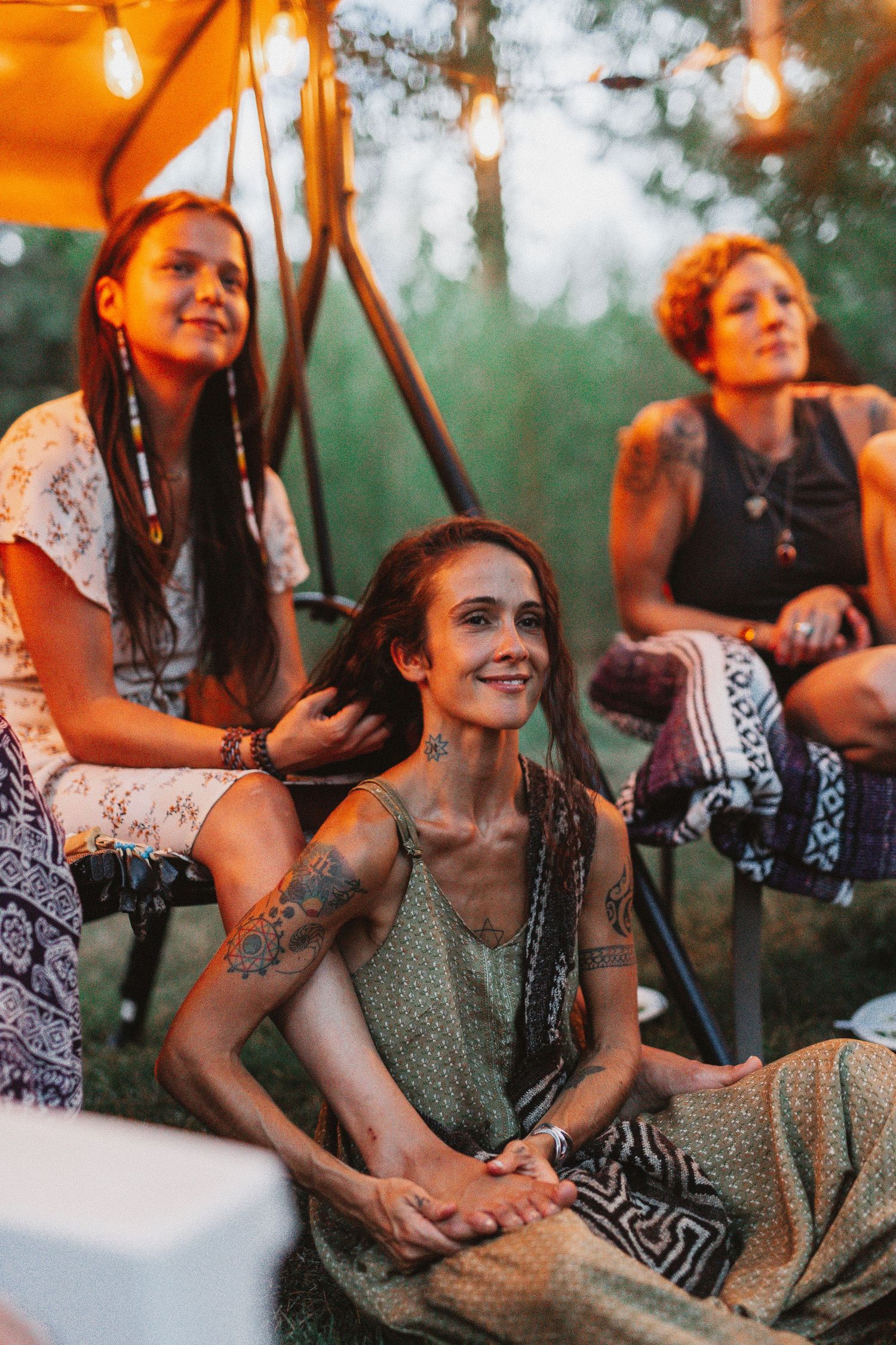 Three friends relaxing under warm lighting at an outdoor bohemian gathering.