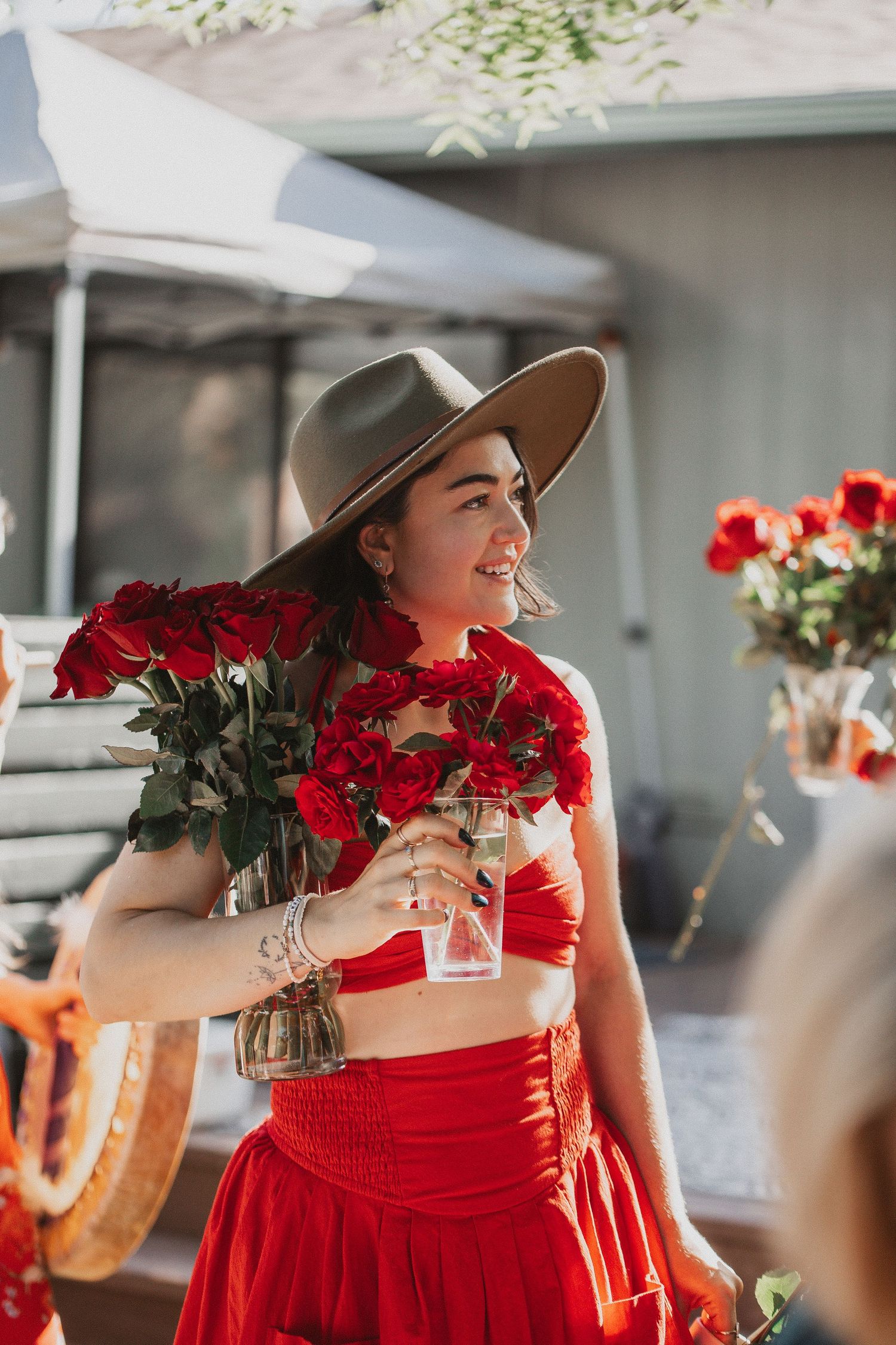 A figure in a vibrant red dress holding red roses while socializing at an elegant outdoor event.