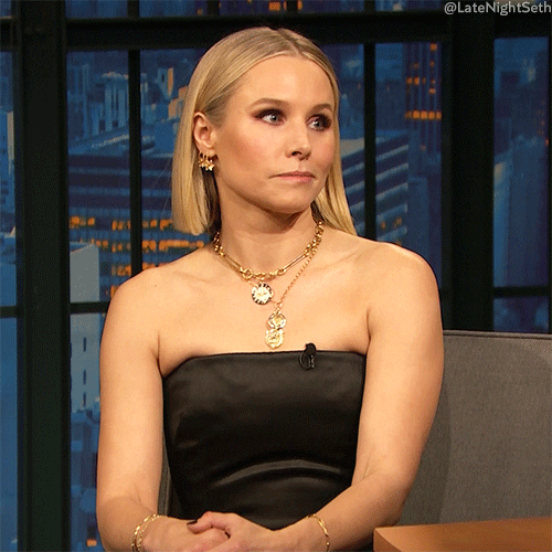 Woman in black strapless dress with layered gold necklaces during television interview.