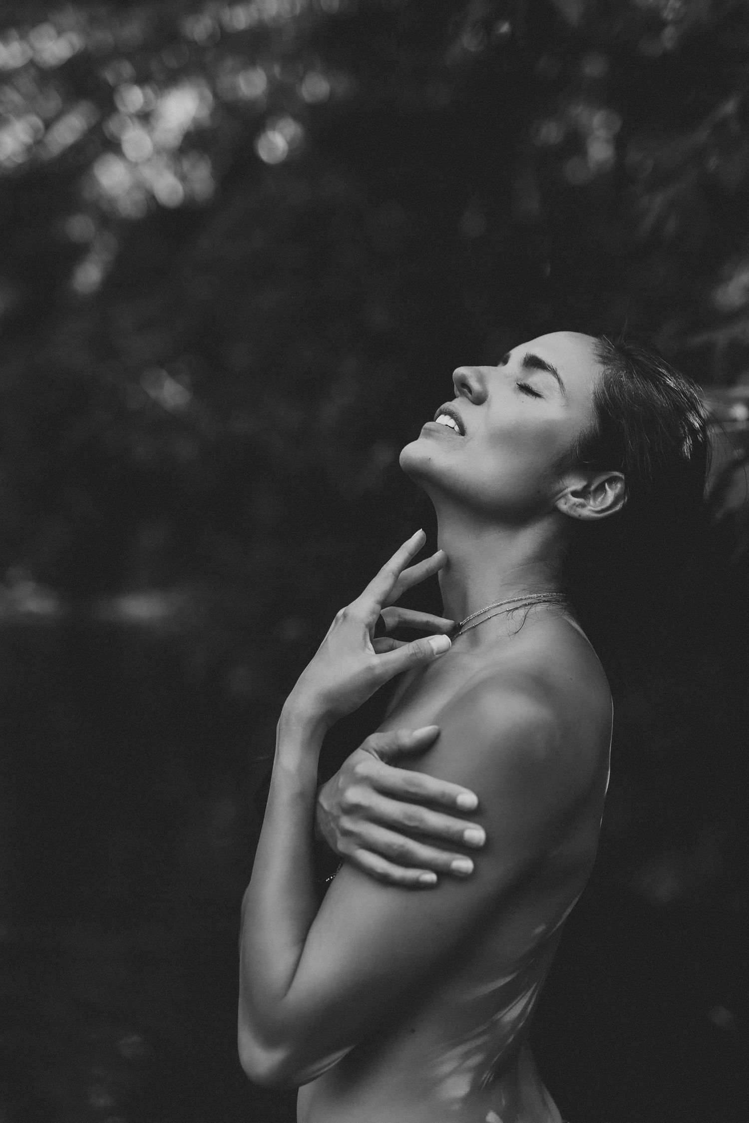 Black and white artistic portrait showing silhouette with head tilted back and hands gracefully touching neck in natural light.