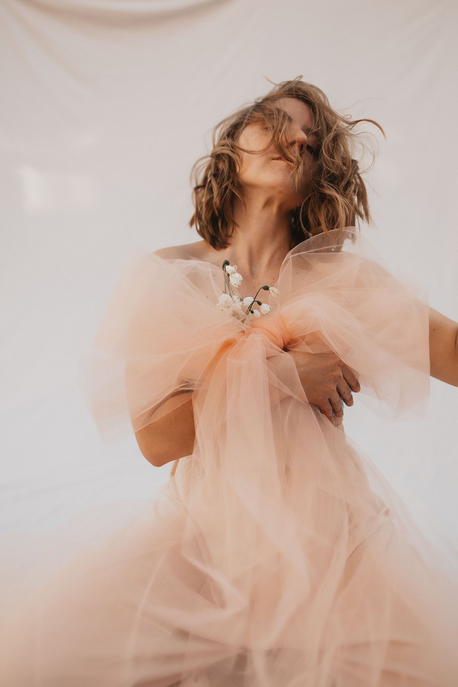 Ethereal fashion portrait with flowing peach tulle fabric and soft romantic lighting against a light backdrop.