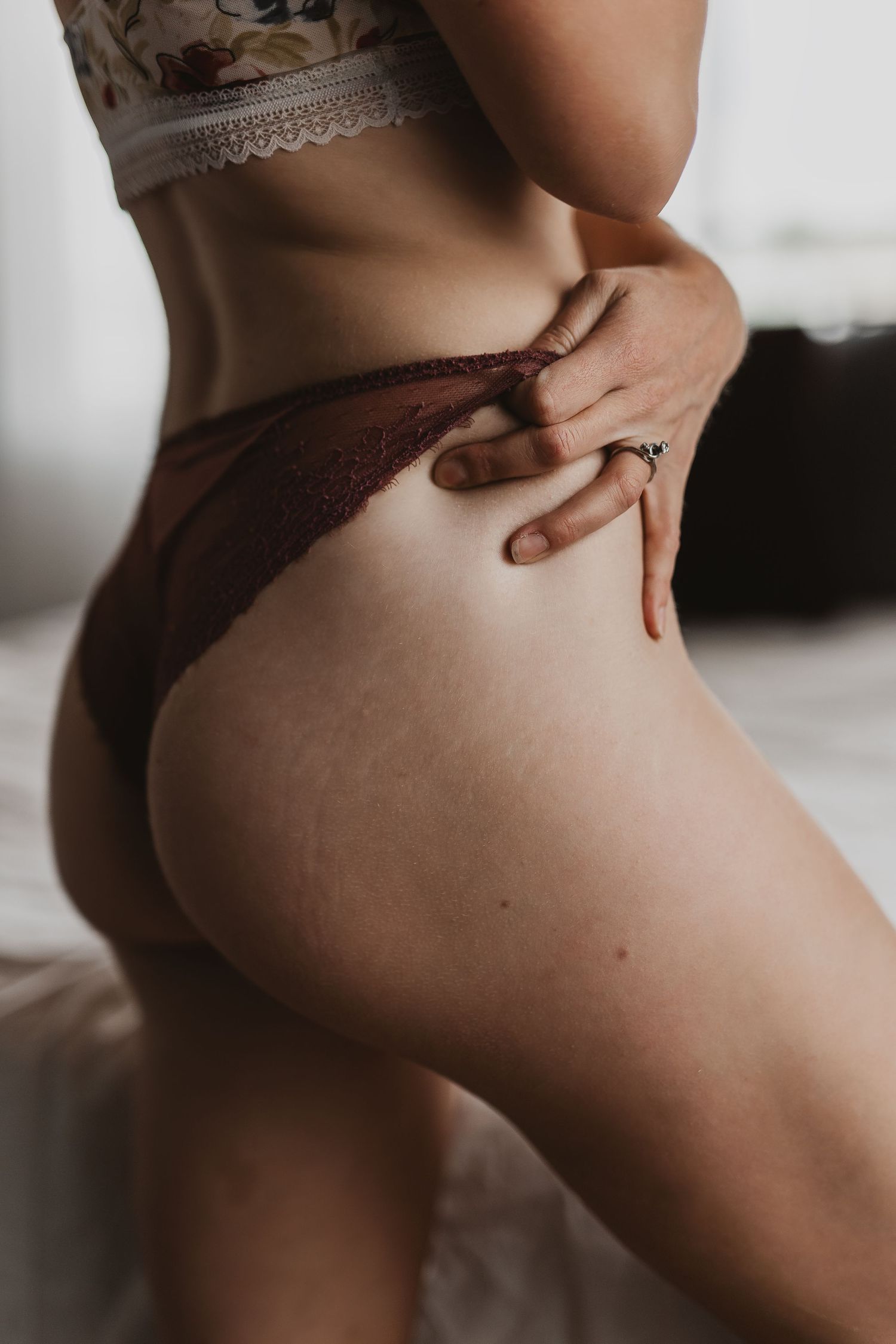 Close-up boudoir photograph showing someone wearing brown lace lingerie in soft natural lighting.