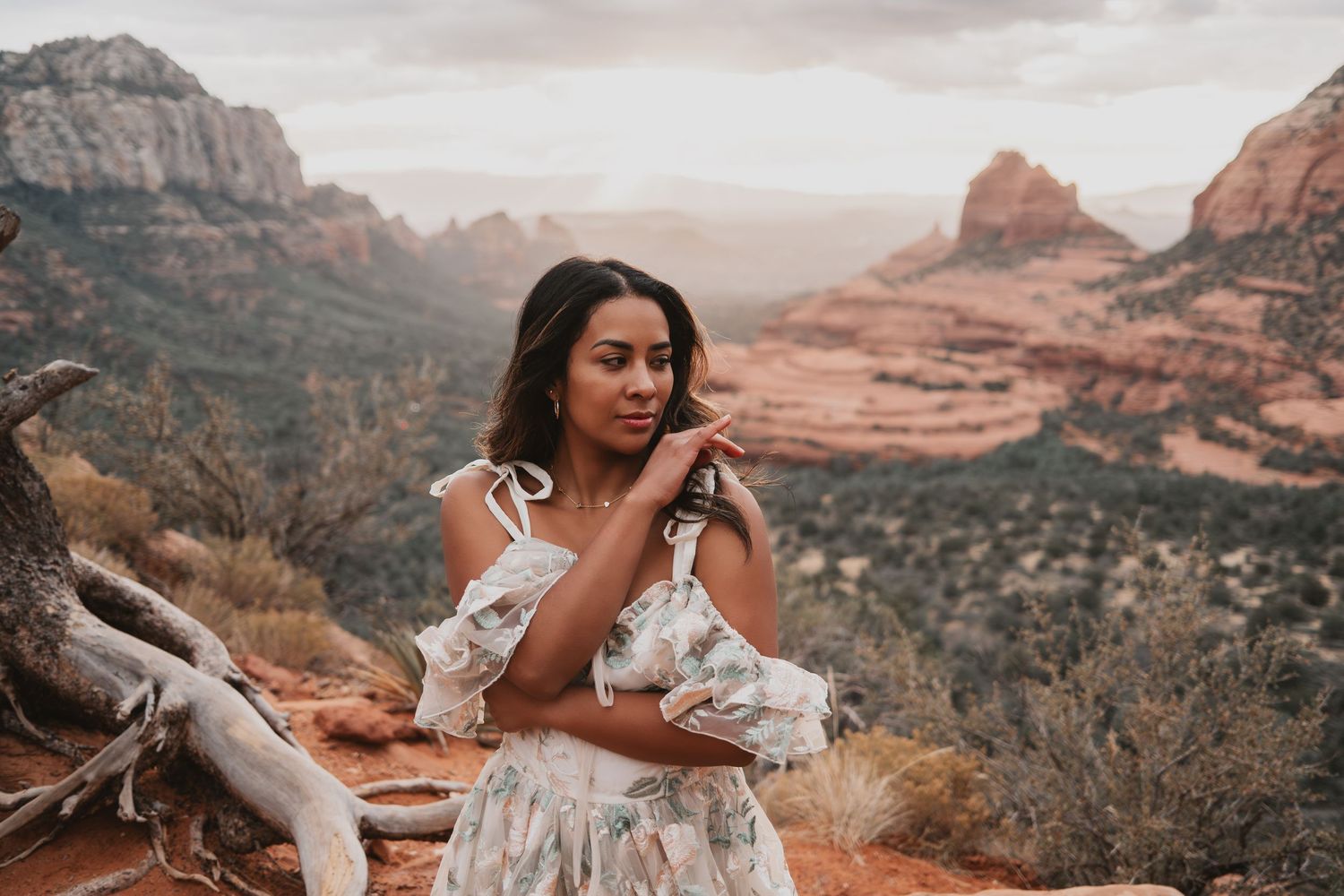 Woman in floral dress posing at Sedona red rock canyon overlook during golden hour sunset.