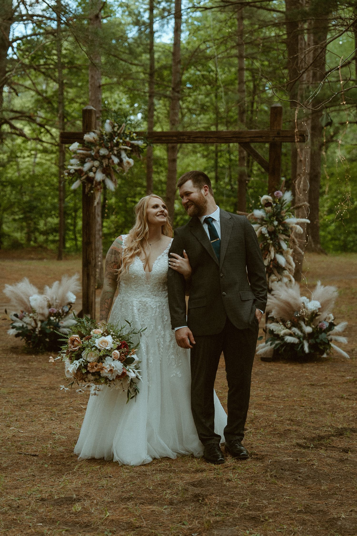 Bride and groom smiling together outdoors in a forest wedding ceremony with pampas grass arch decor.