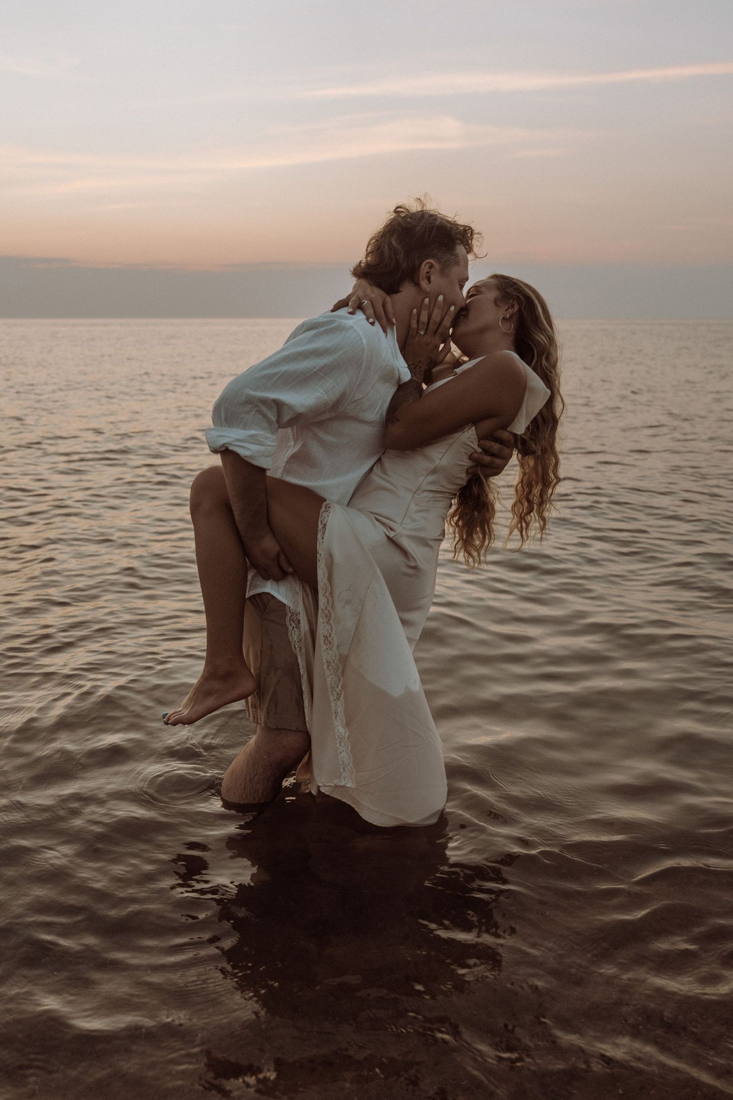 A couple embraces in shallow ocean waters during sunset creating a romantic silhouette against the horizon.