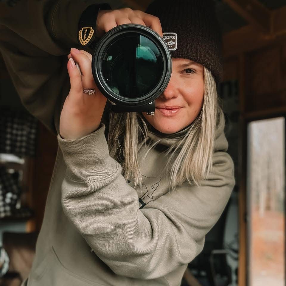 Photographer in beige sweater holding camera in multiple similar poses against wooden interior background.