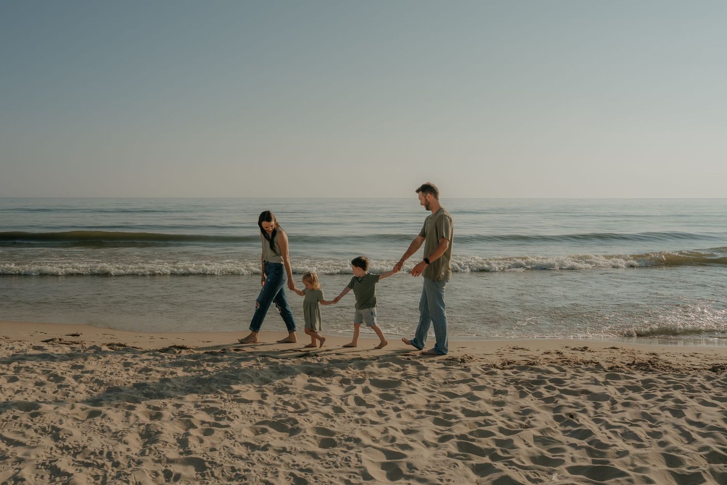 Family walking together along a scenic beach shoreline at sunset with waves crashing in the background.