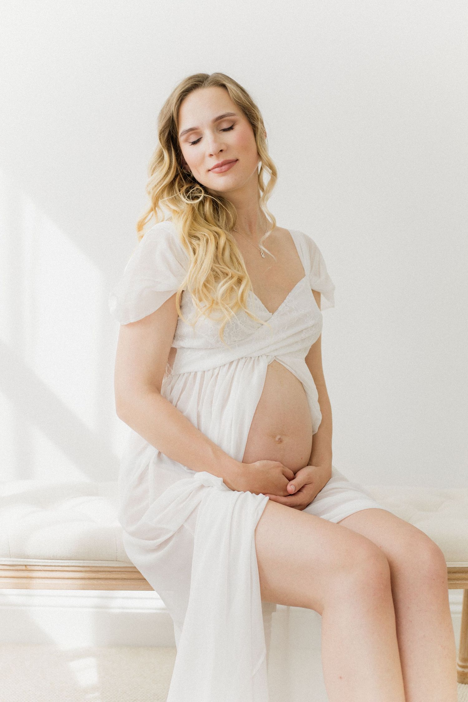 Intimate maternity boudoir session with soft white fabrics in natural window light.