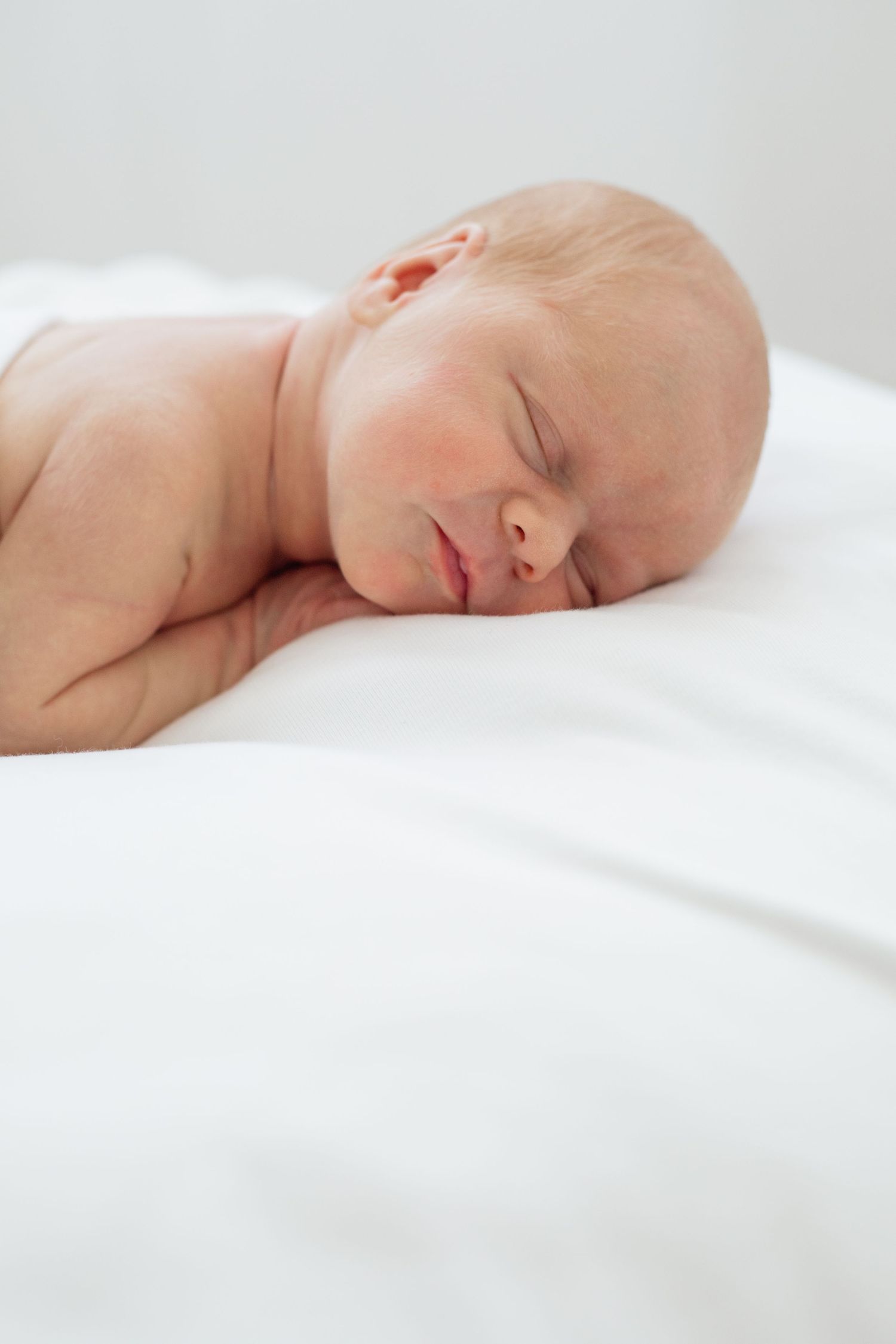Peaceful newborn baby sleeping on white bedding in natural light.