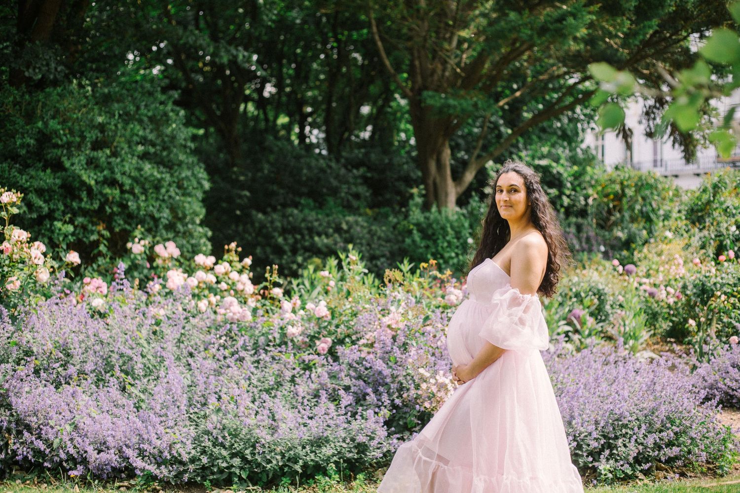 A romantic maternity photo session in a garden with lavender flowers and soft natural lighting.