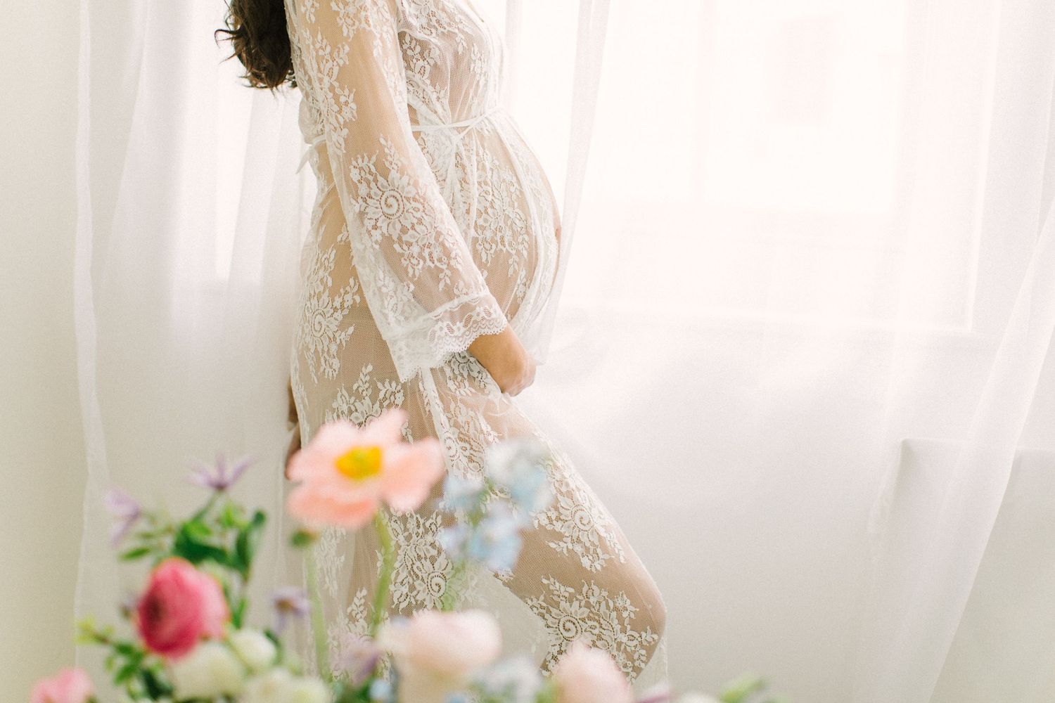 Elegant lace maternity gown with colourful floral accents in bright studio.