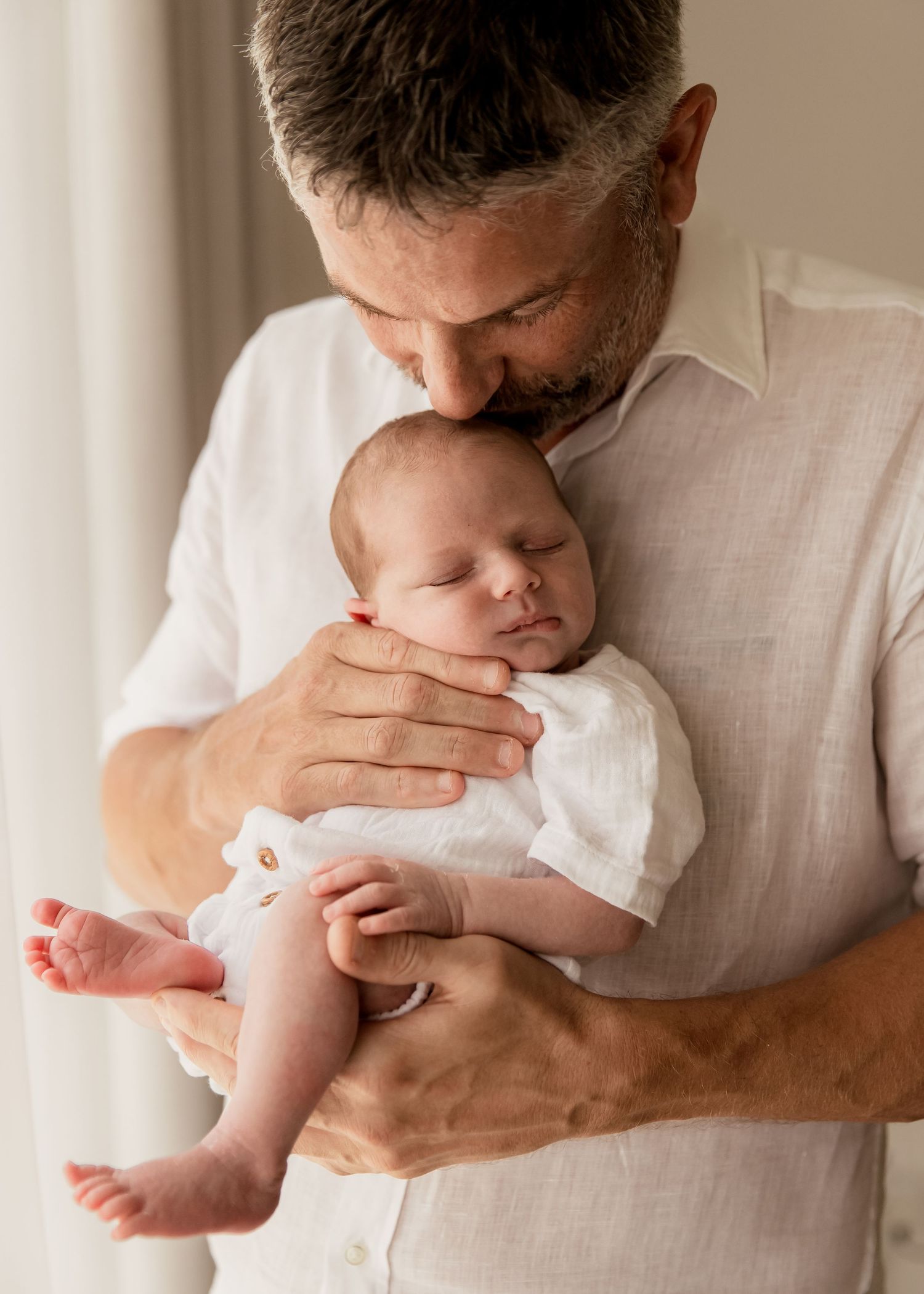 Father holding newborn baby close to his chest and kissing his head tenderly during at-home lifestyle newborn photoshoot in Dubai